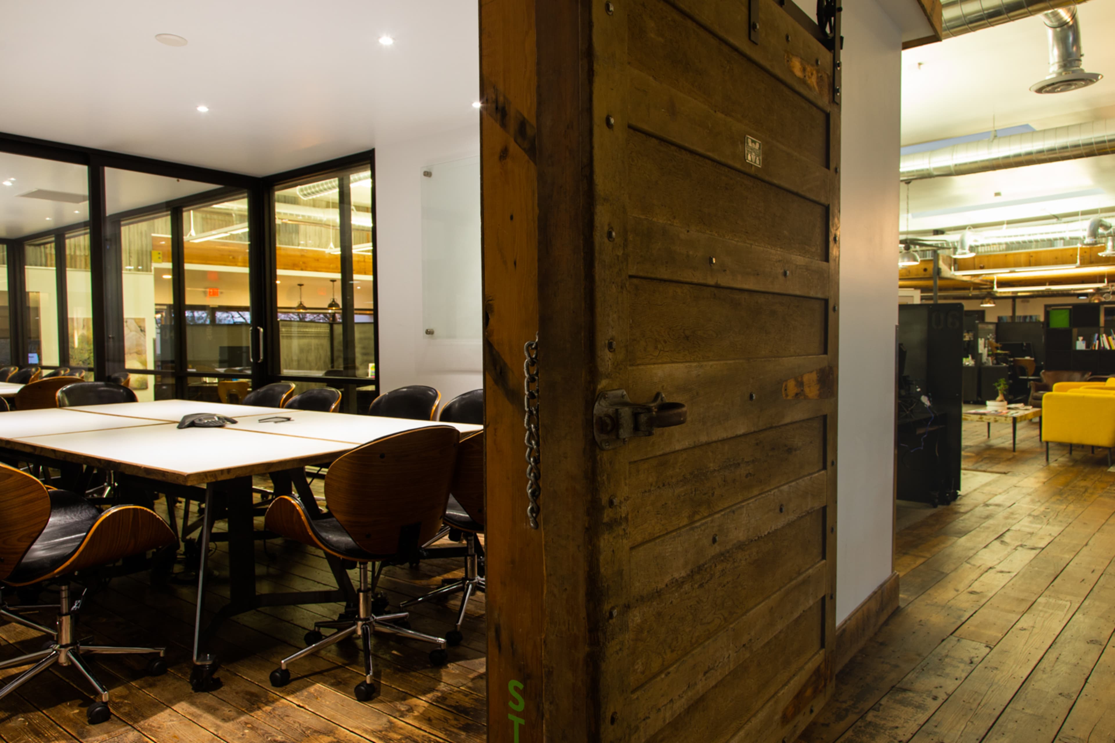 A wooden door partially open, revealing a modern conference room with a large table and ergonomic chairs.