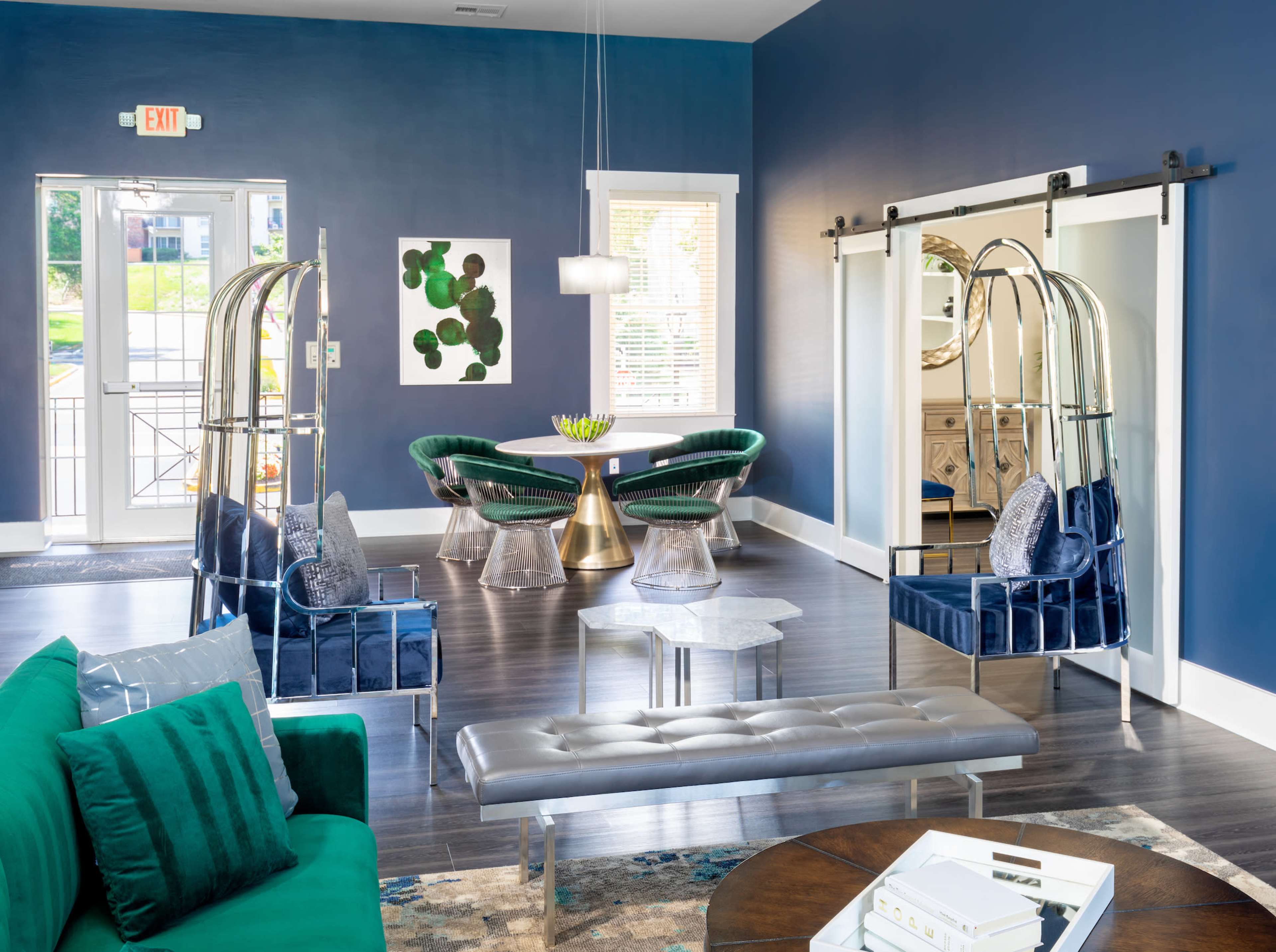 A modern lounge area with blue walls, green seating, and stylish furniture, including a round dining table and unique swing-style chairs.