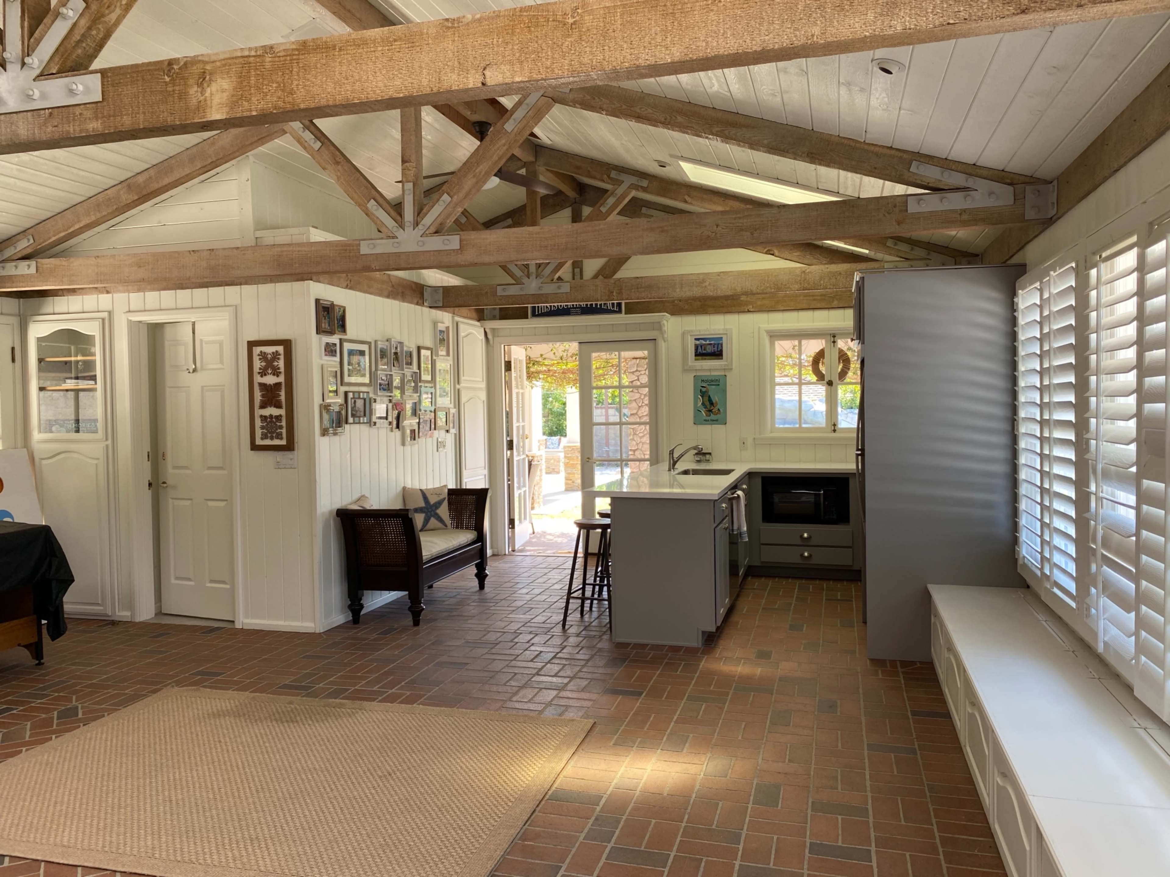 A spacious interior of a kitchen and living area with exposed wooden beams, tile flooring, and large windows letting in natural light.
