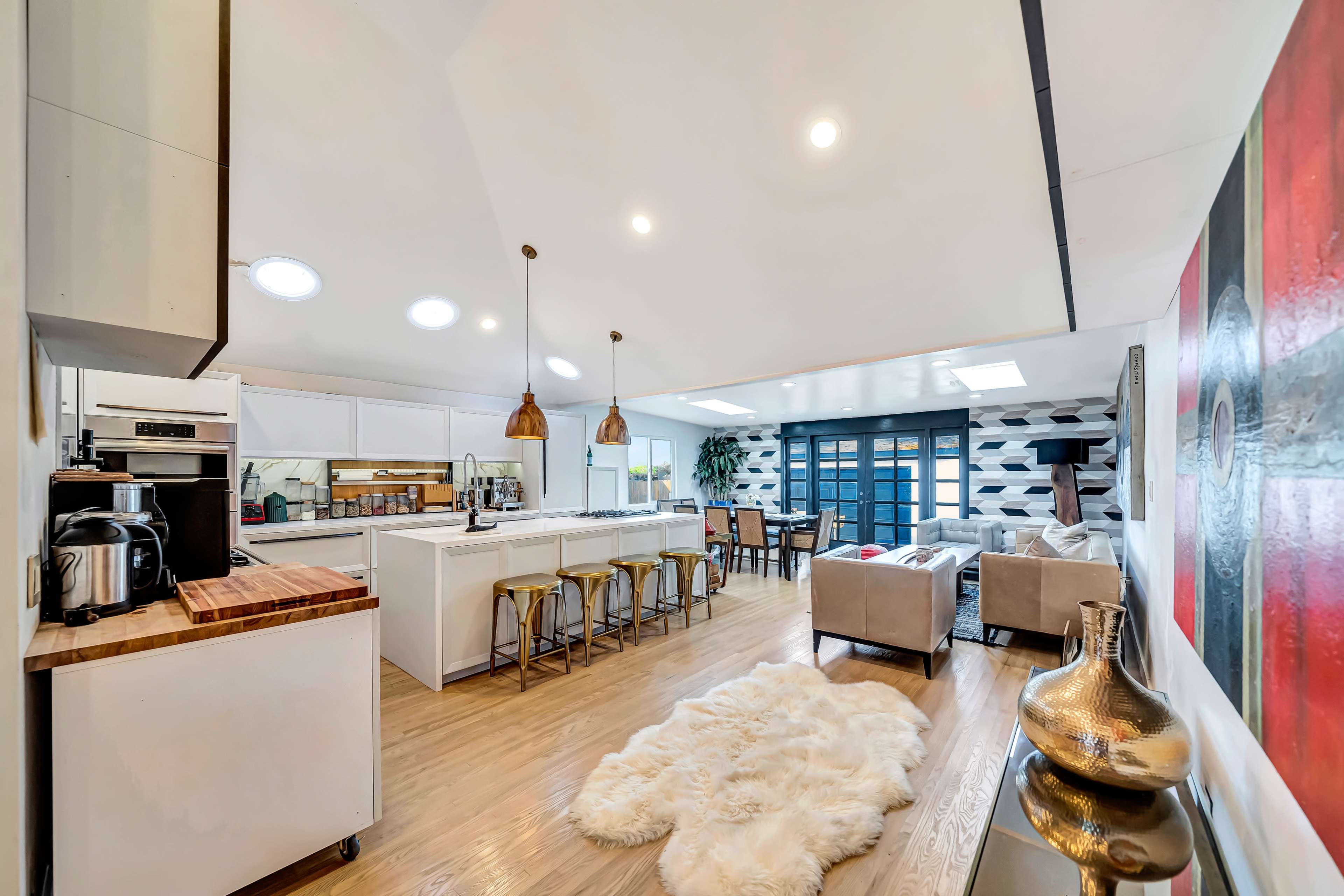 A modern open-concept living space with a kitchen, dining area, and lounge featuring a large window and minimalist decor.