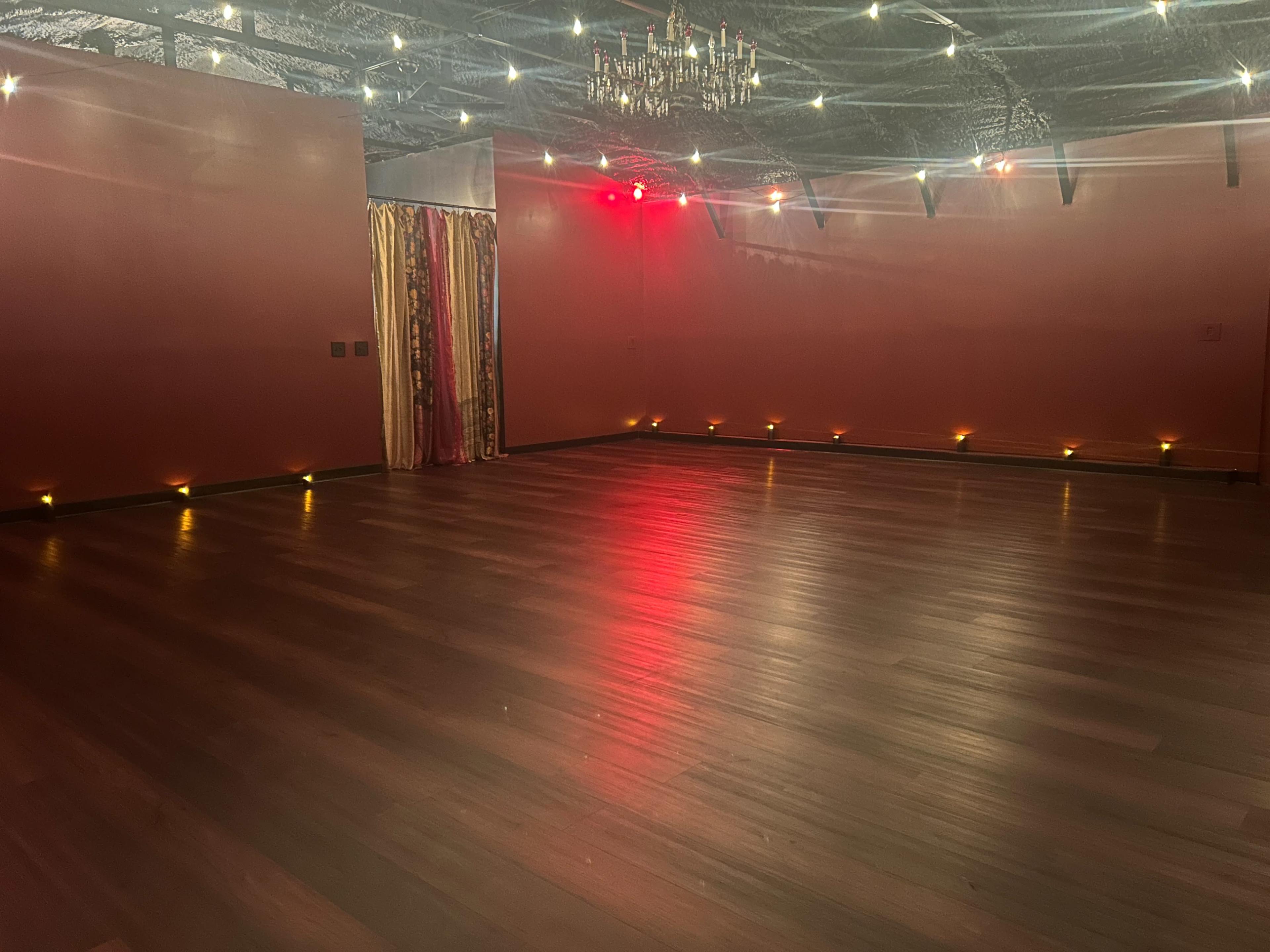 The image shows a spacious room with wooden flooring, dim lighting, and decorative curtains on one wall.