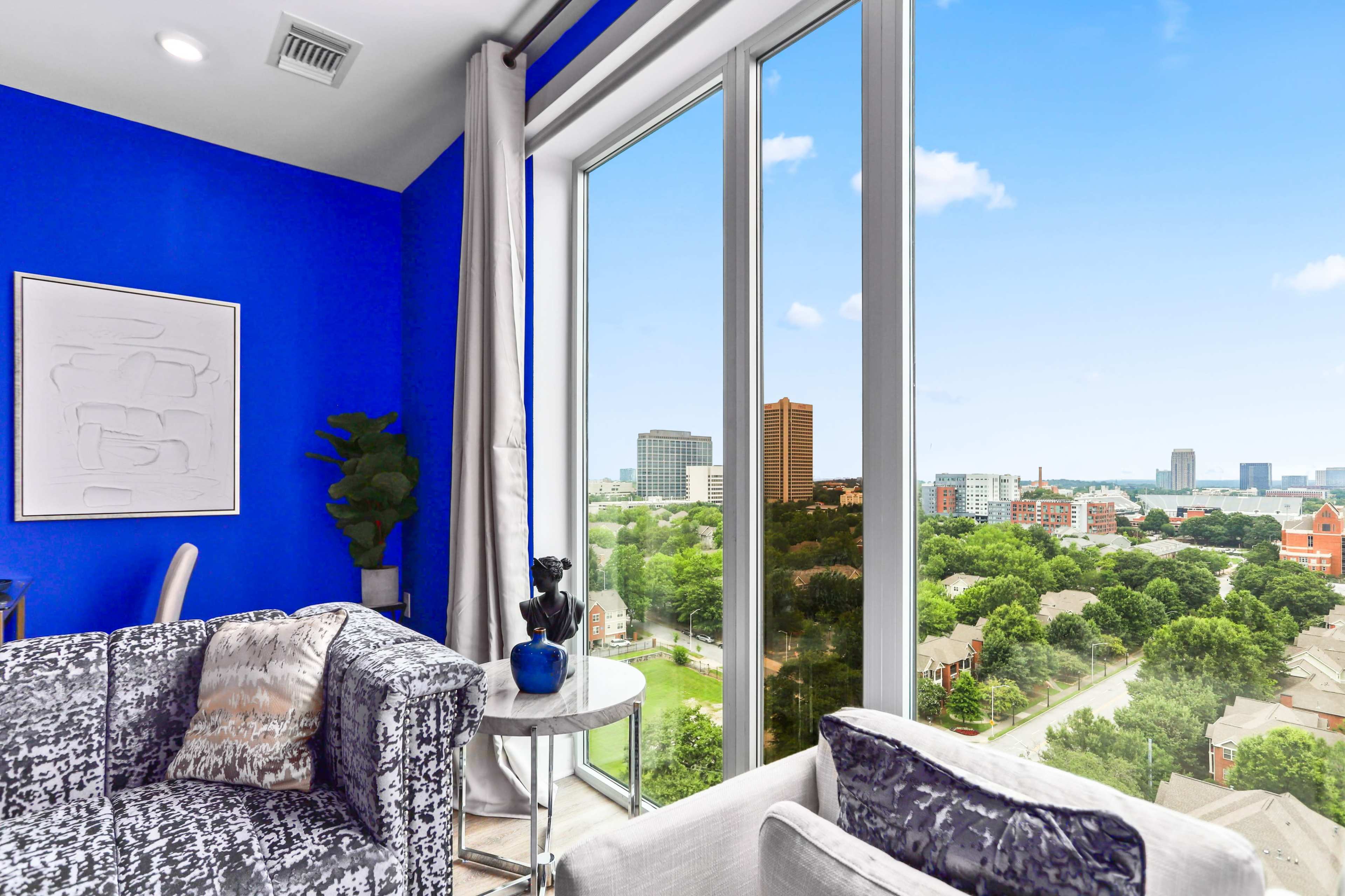 A modern living space features large windows offering a view of a city skyline, with blue walls and contemporary furniture.