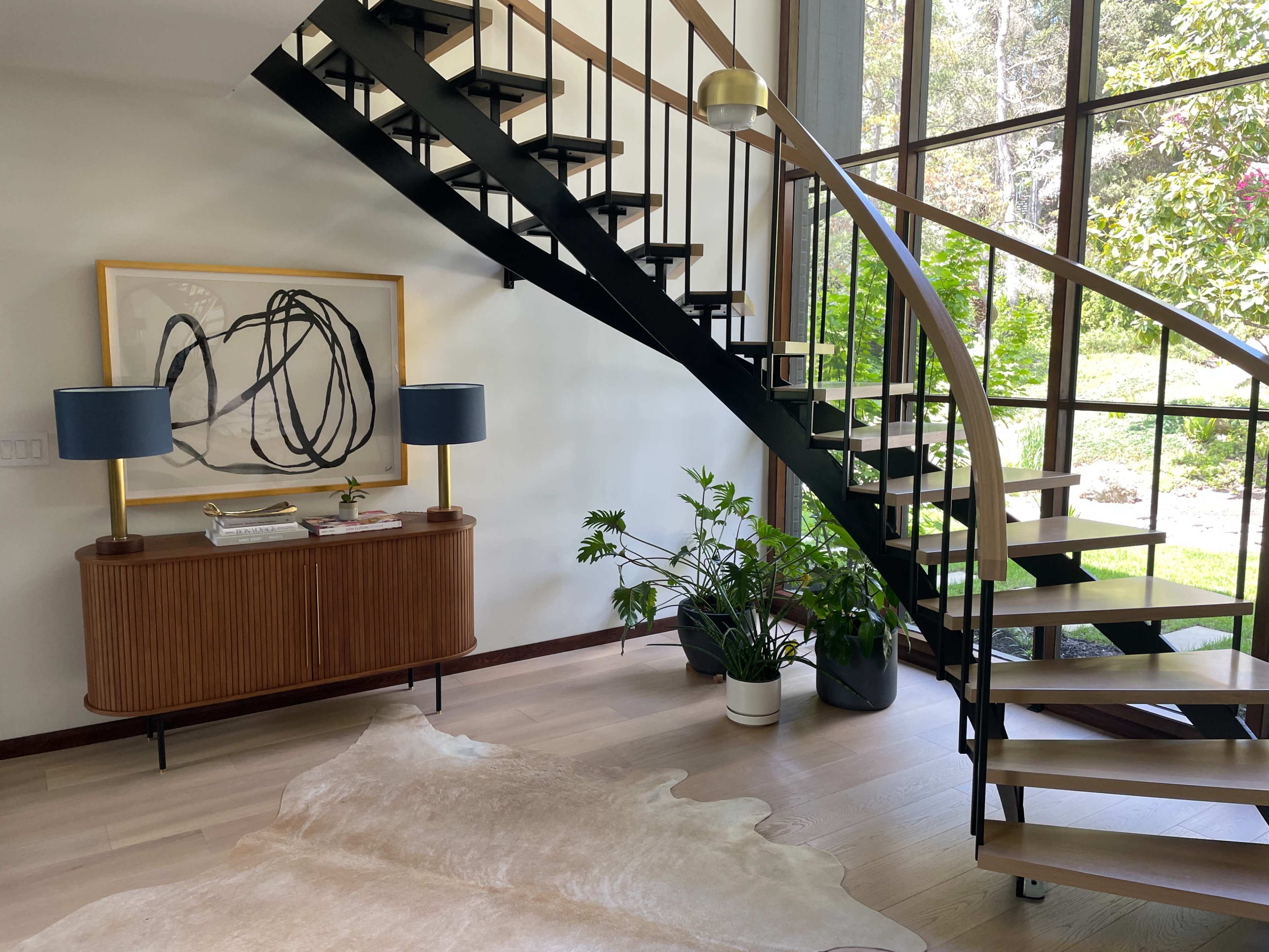 A spiral staircase leads from a modern entryway to a bright space filled with plants and natural light.