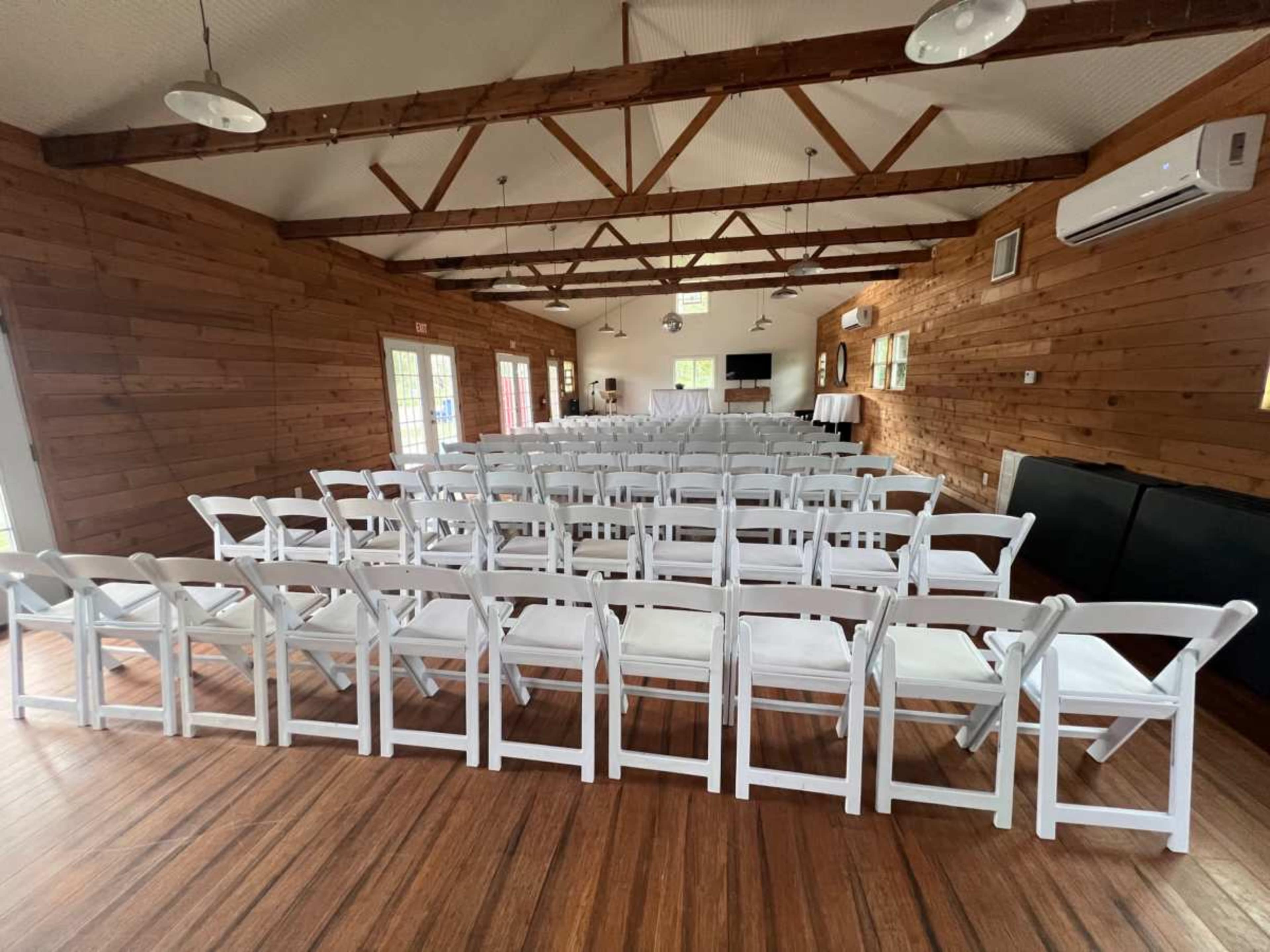 The image shows a spacious room with wooden walls and a set of white folding chairs arranged in rows facing a front area.
