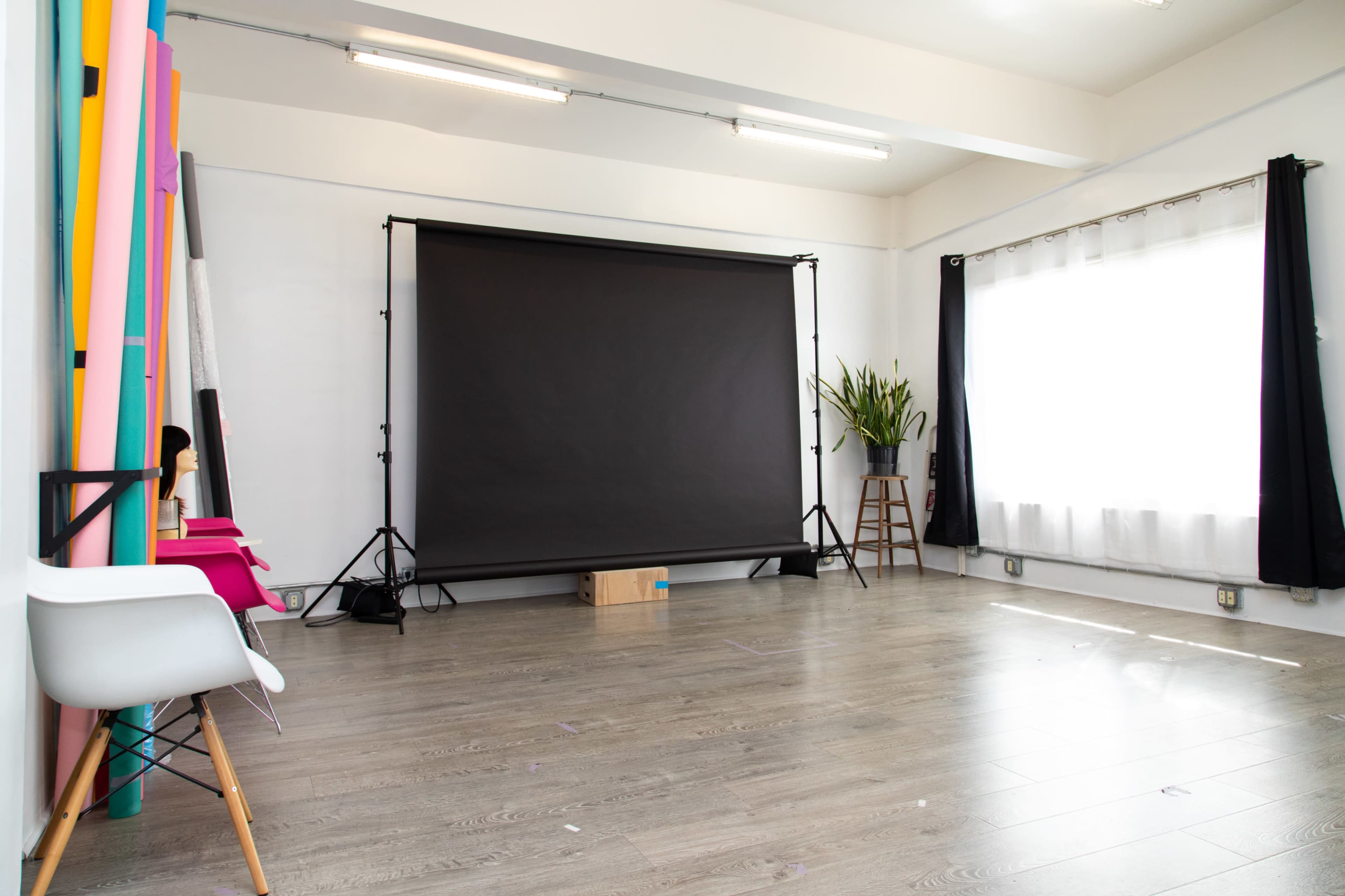 A spacious studio features a black backdrop, wooden flooring, and colorful backdrop rolls arranged against the wall.