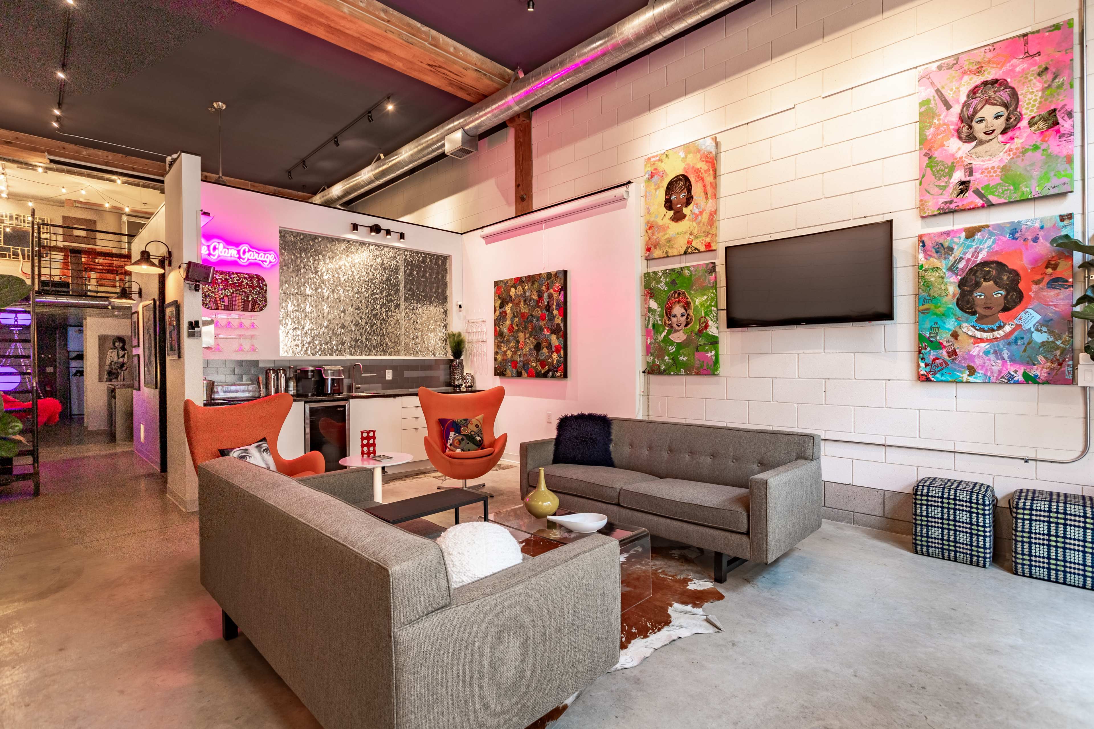 The image depicts a modern lounge area with two sofas, colorful artwork on the walls, and a bar area in the background.