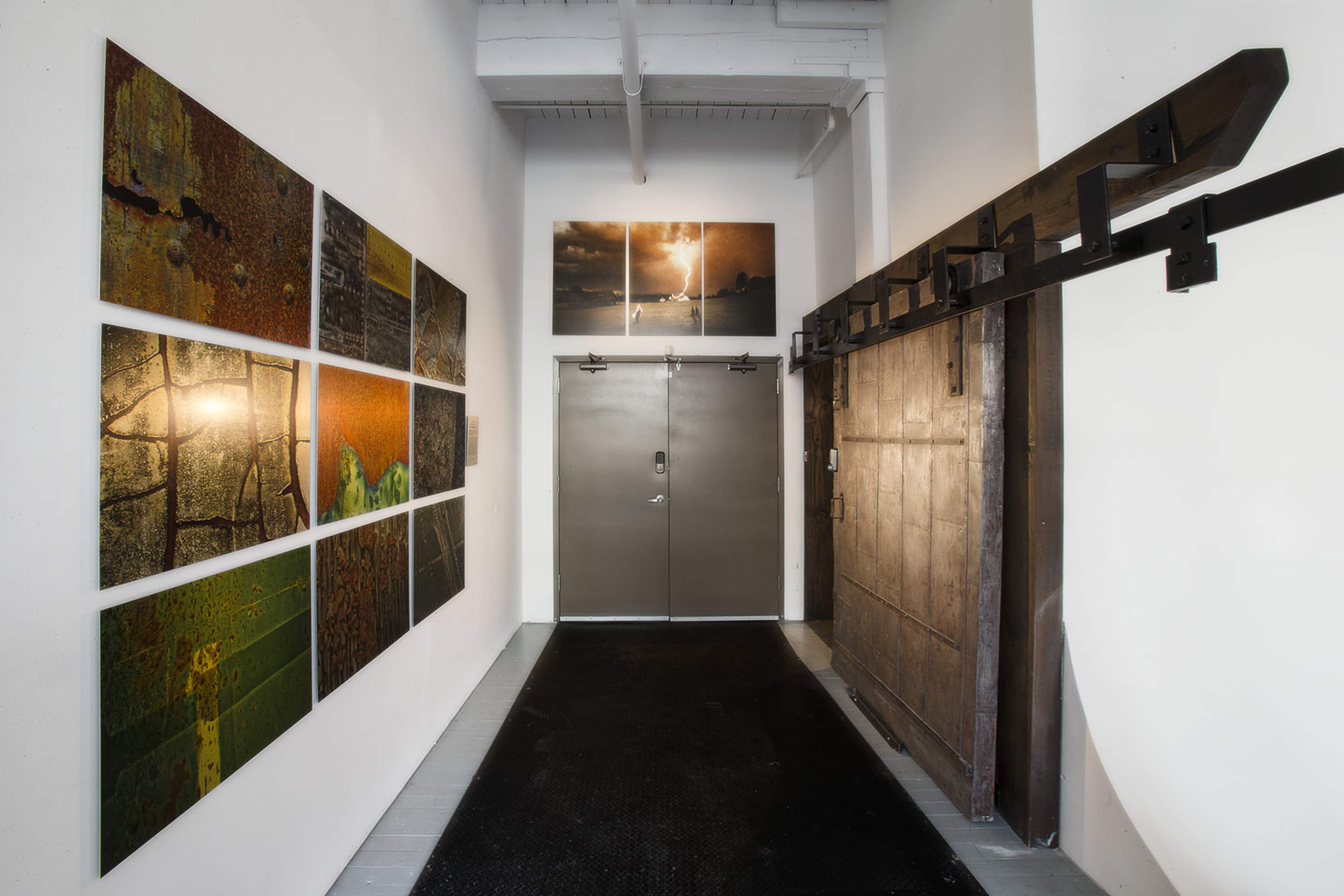 An interior hallway featuring large wall-mounted artwork, a pair of double doors, and a sliding wooden door on a track.