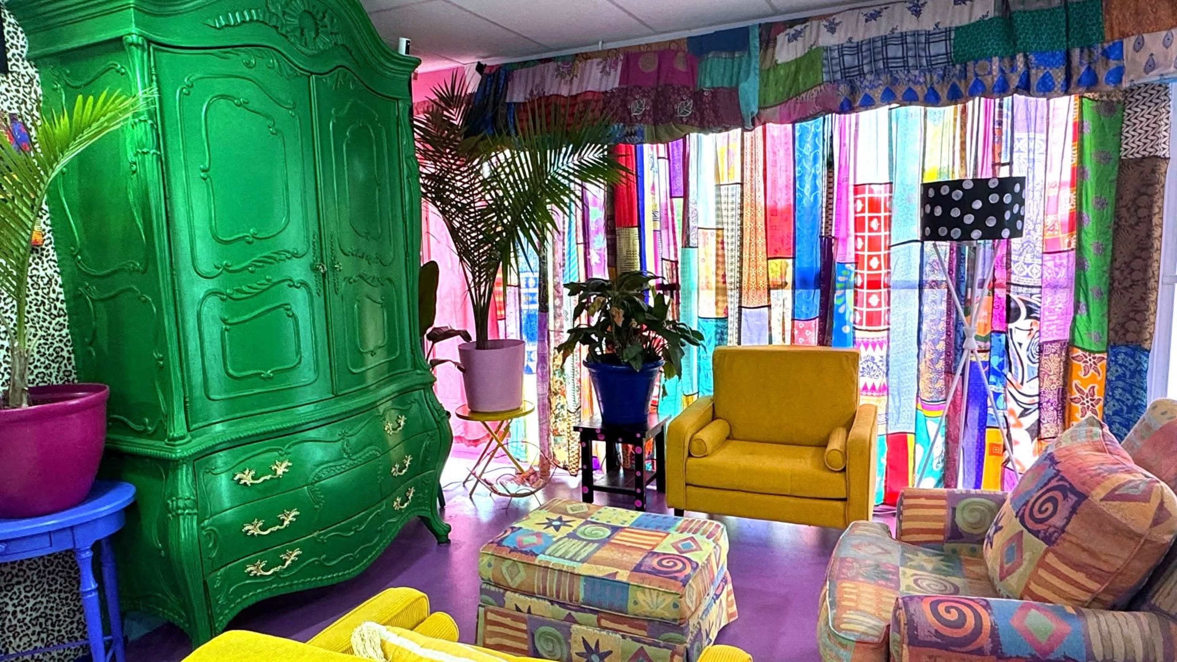 The room features vibrant, colorful decor with a green armoire, yellow chairs, and patterned curtains.