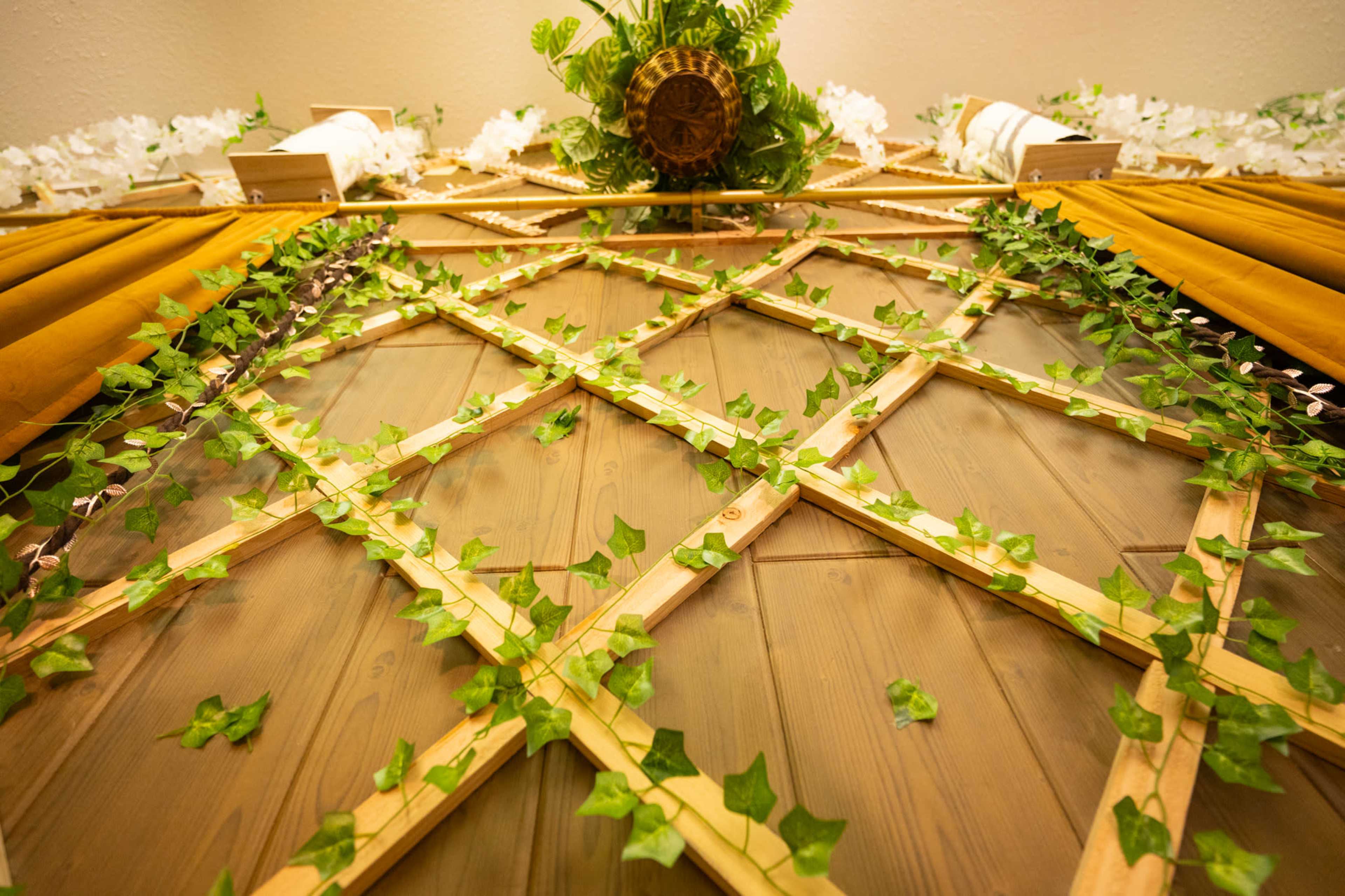 The image shows a wooden lattice decorated with green ivy leaves and floral accents at the top.