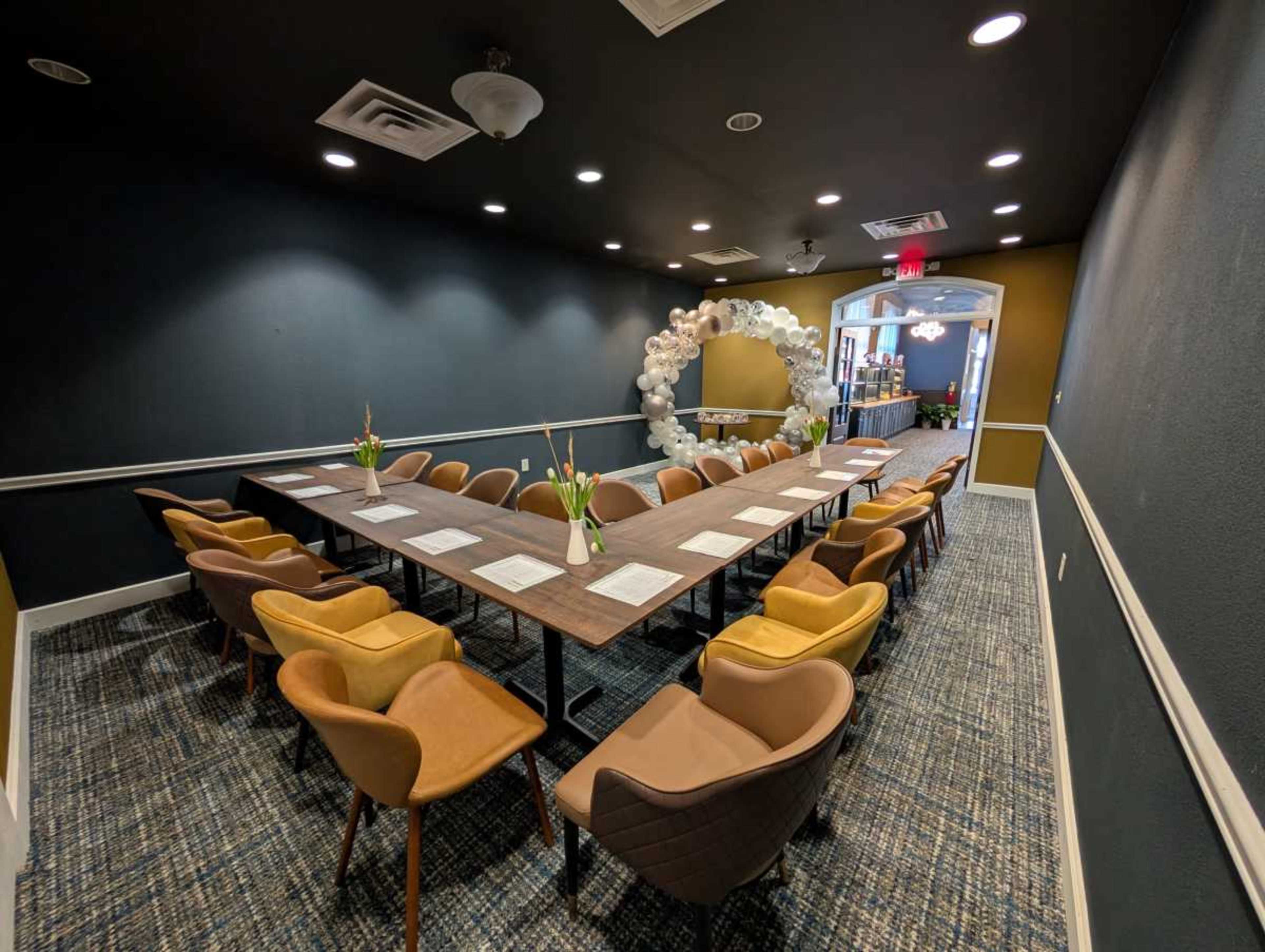 A conference room features a long table surrounded by chairs, with a decorative arch made of balloons in the background.