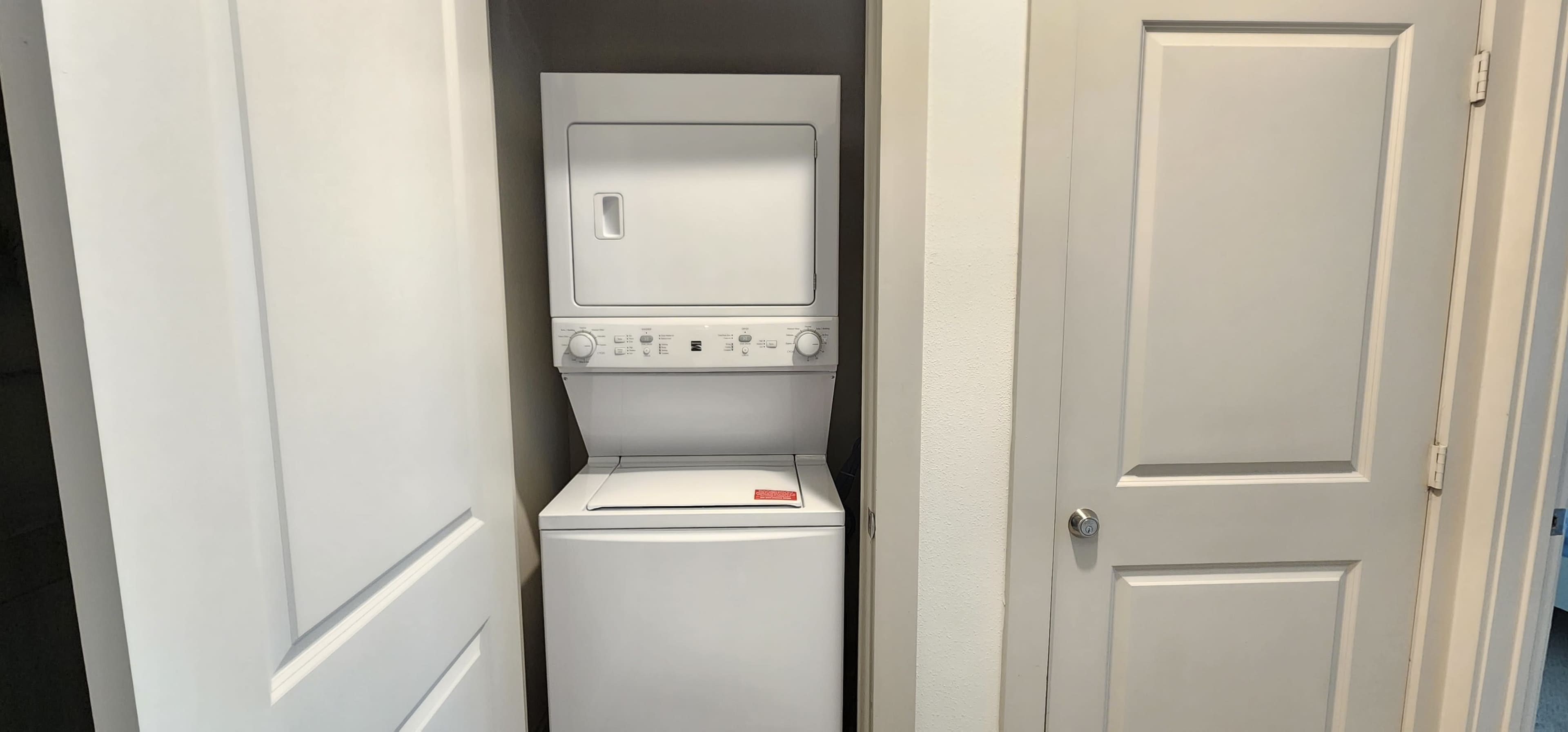 A stacked washer and dryer are located in a narrow closet between two doors.