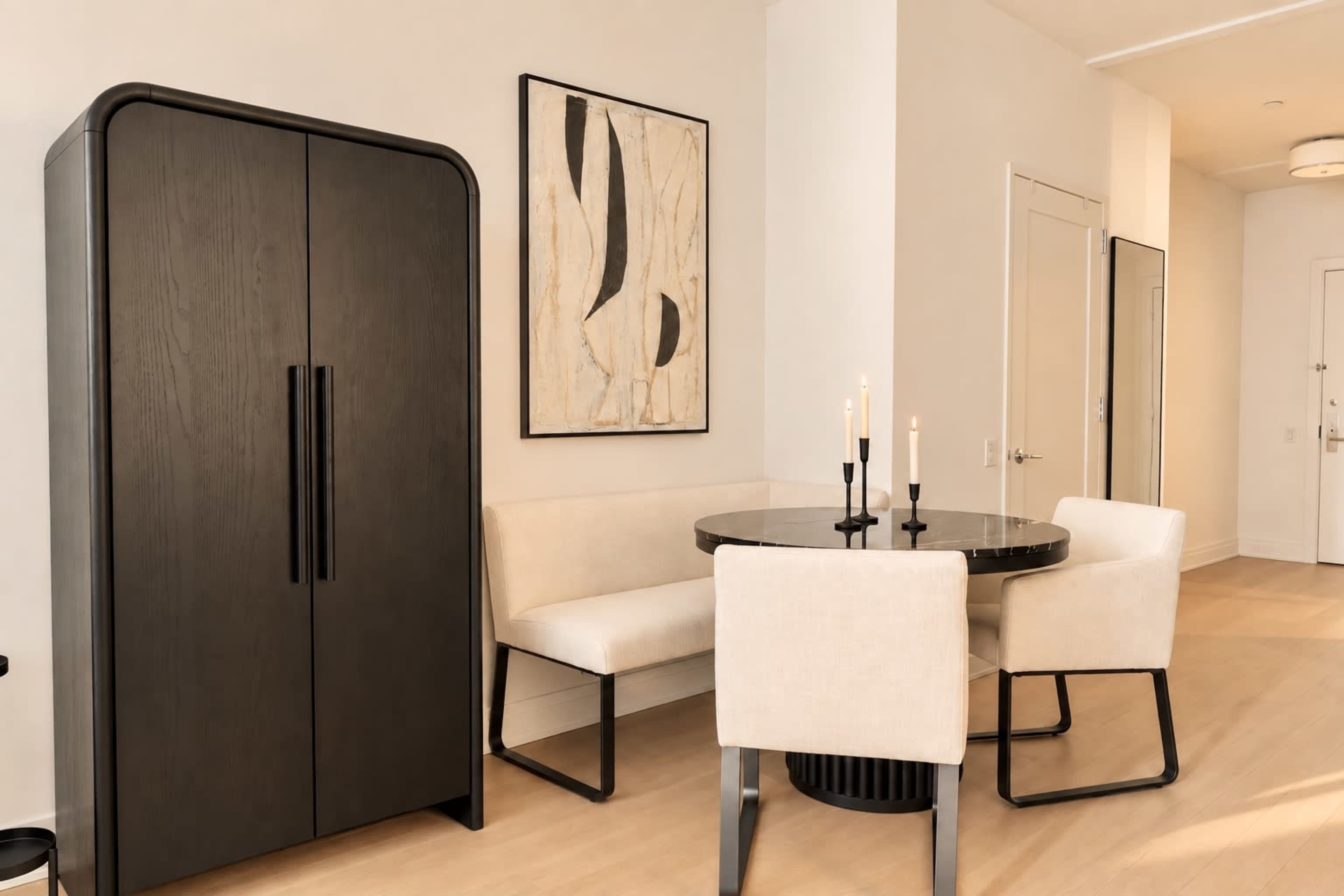 A sleek dining area features a round table surrounded by four upholstered chairs, with a black cabinet and abstract wall art nearby.