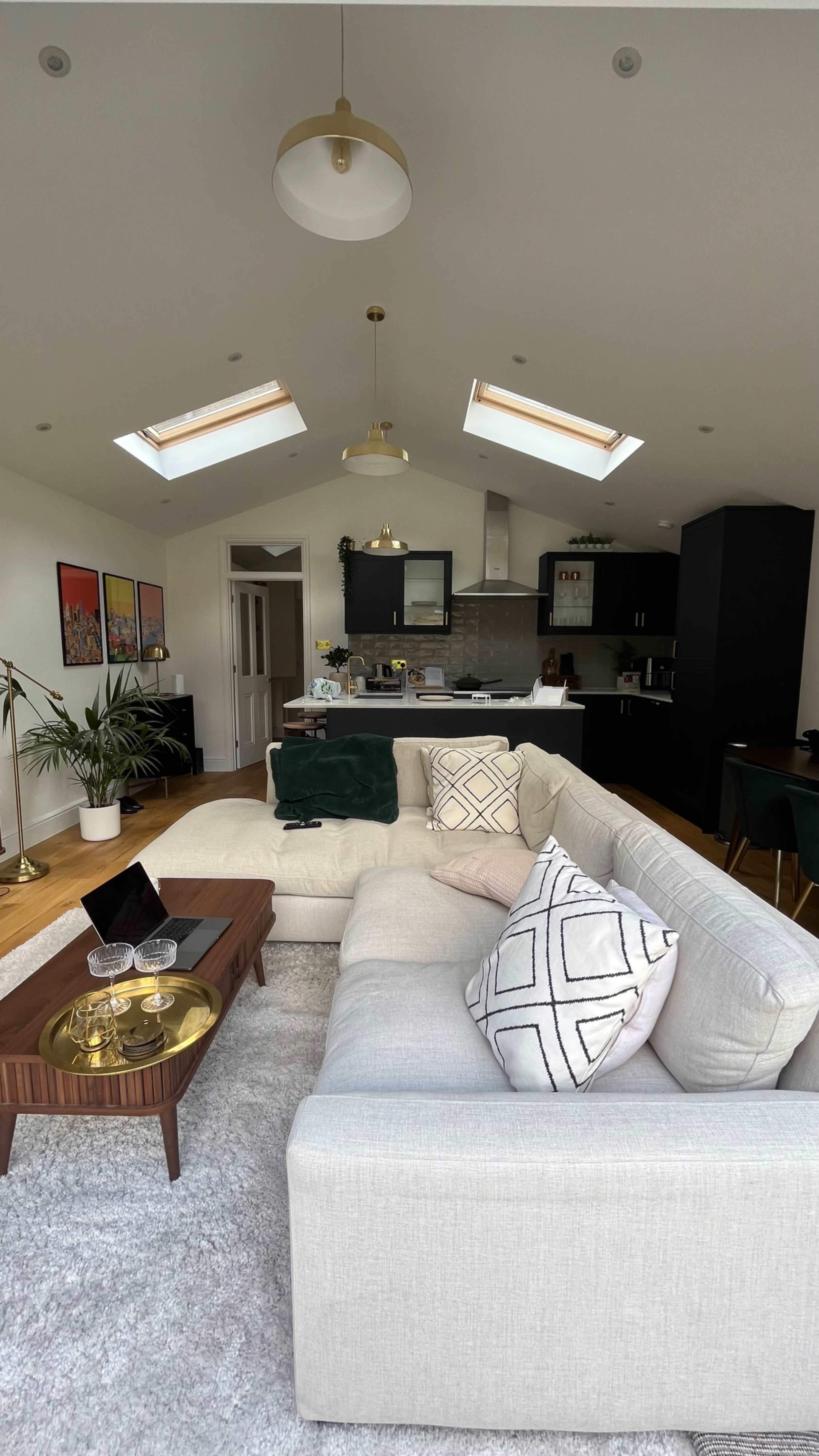 The image shows a modern living room with a large sectional sofa, a wooden coffee table, and an open kitchen area in the background.