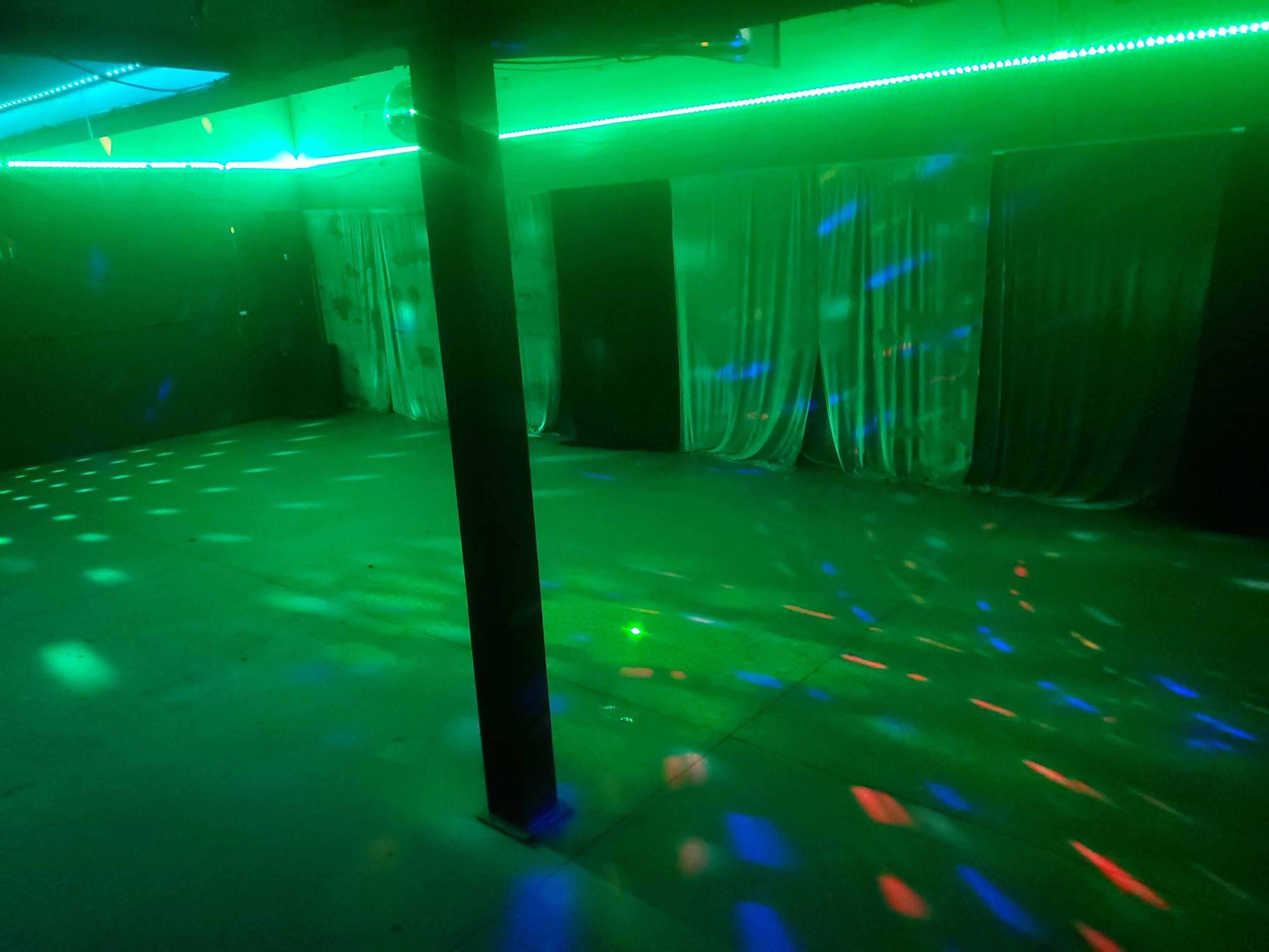 The image shows an empty room with colorful lights reflecting off the walls and floor, illuminated by green lighting and a disco ball effect.