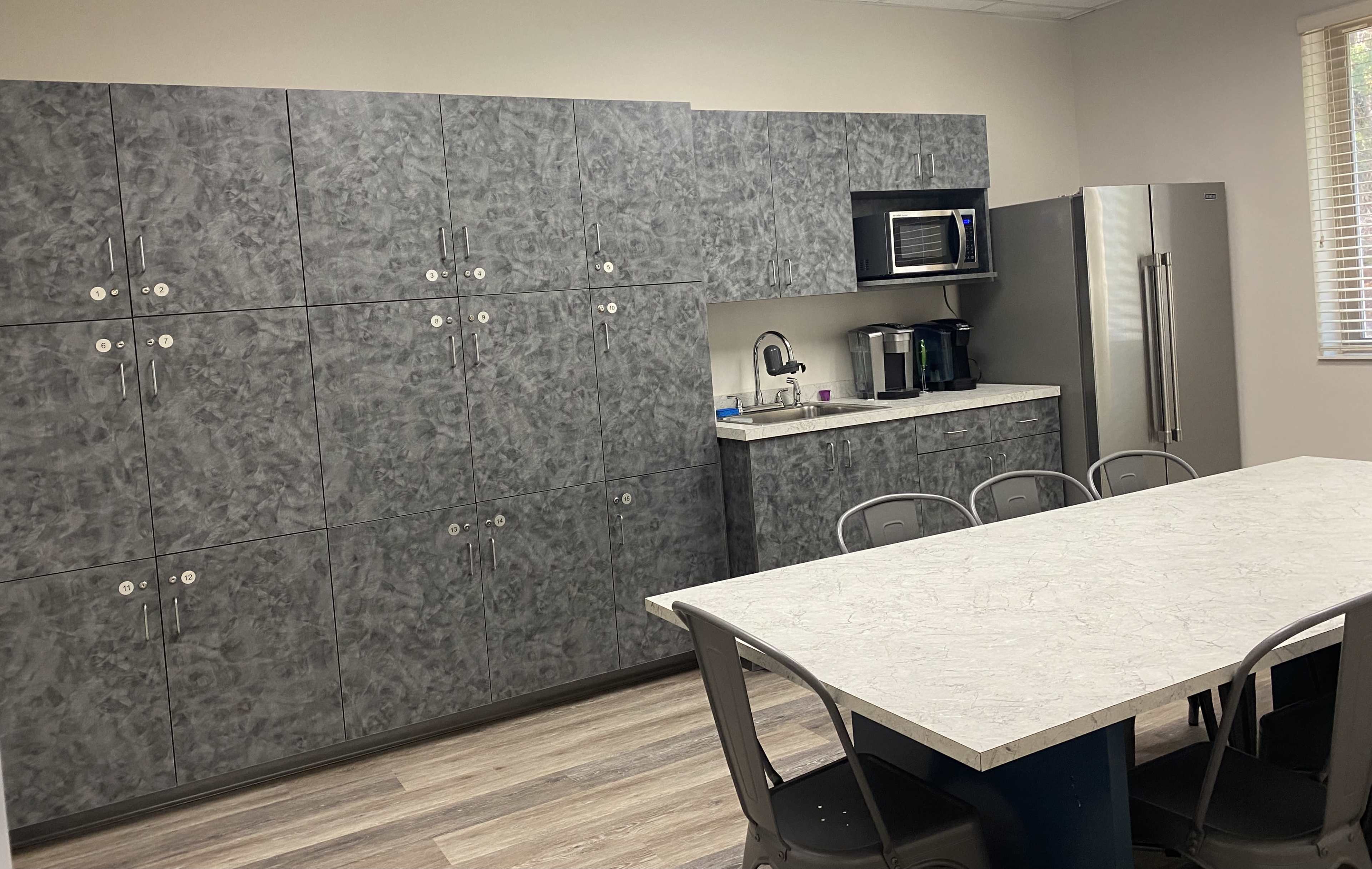 A modern kitchen with gray cabinets, a countertop, a microwave, a coffee maker, and a dining table with metal chairs.