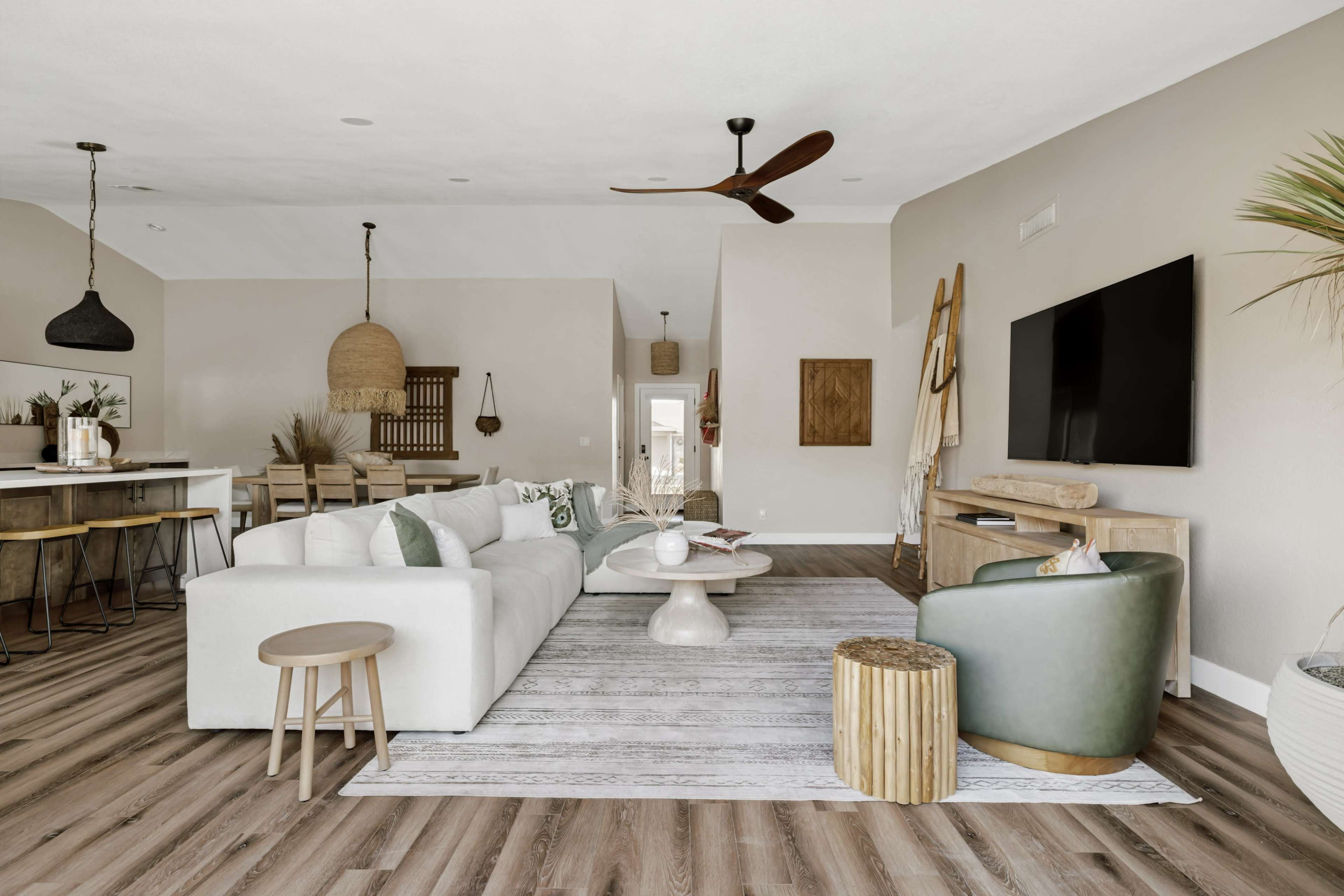 The image depicts a modern living room with a light-colored sofa, a coffee table, and a television mounted on the wall, all set against a backdrop of wooden flooring and neutral walls.
