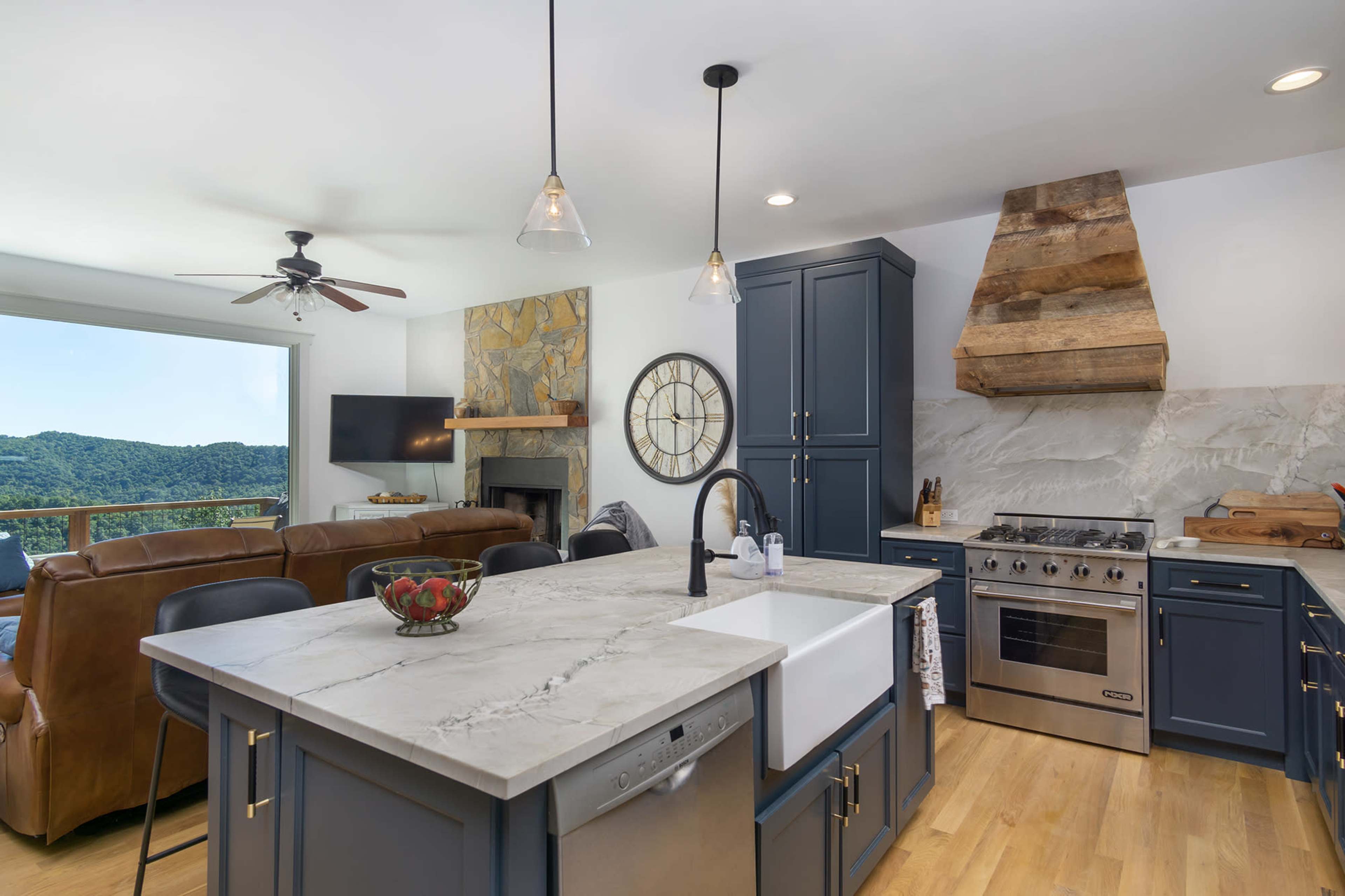 A modern kitchen with a large island, stainless steel appliances, and a view of a mountainous landscape through sliding glass doors.