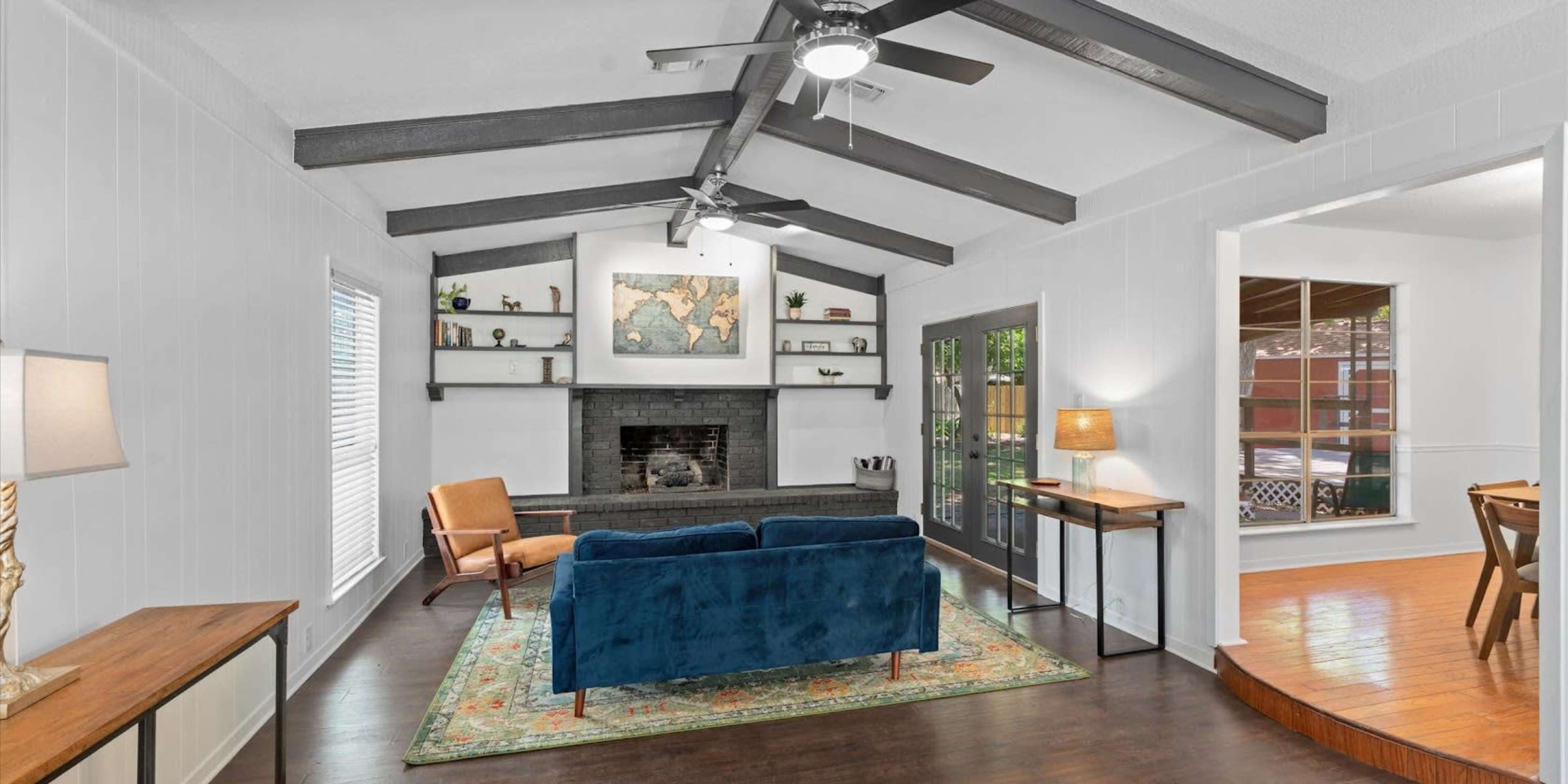 A living room with a blue couch, a black fireplace, and high, exposed beam ceilings, along with bookshelves and a large map hanging on the wall.