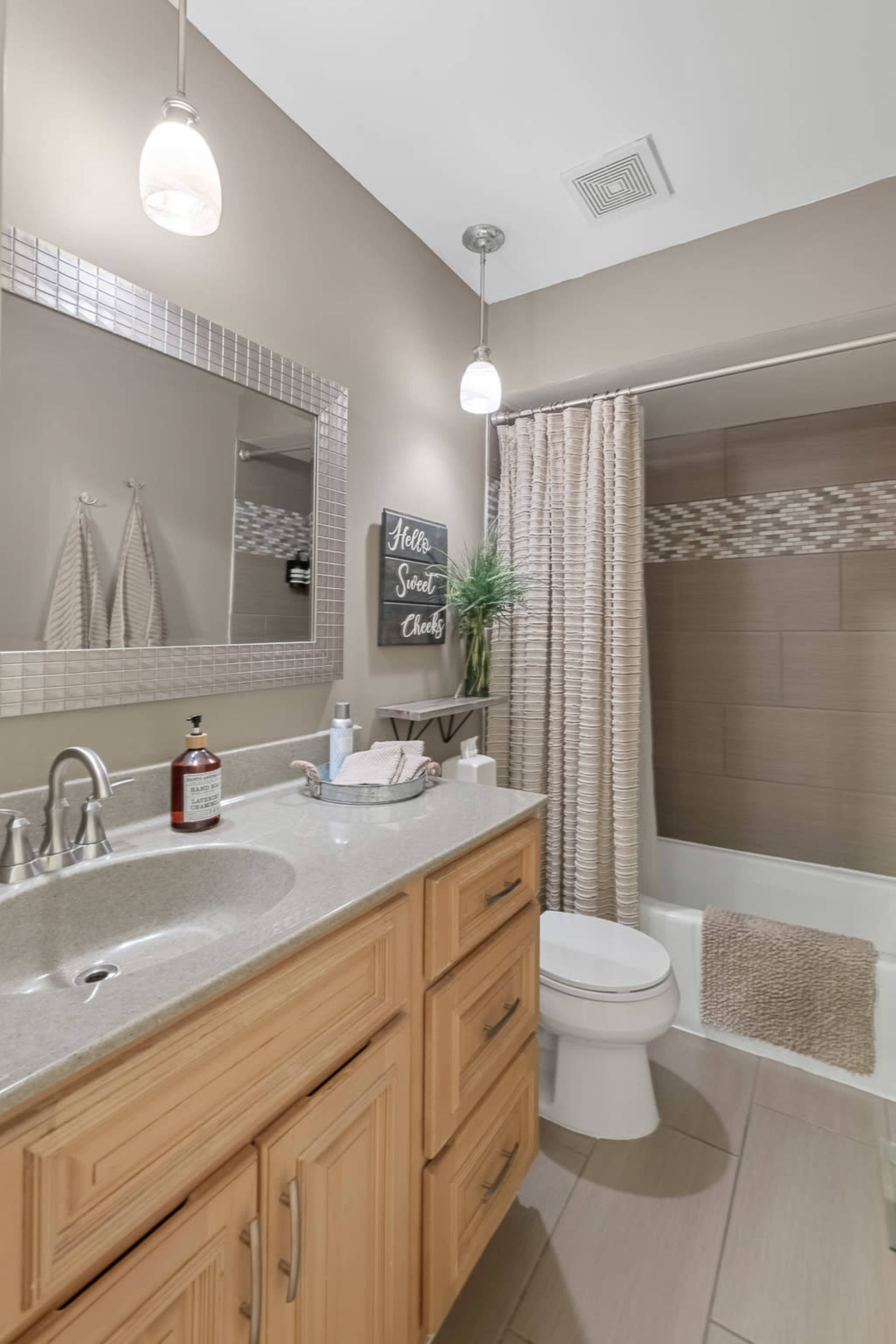A modern bathroom features a single sink with an oak vanity, a large mirror, a shower-tub combo with a decorative curtain, and overhead lights.