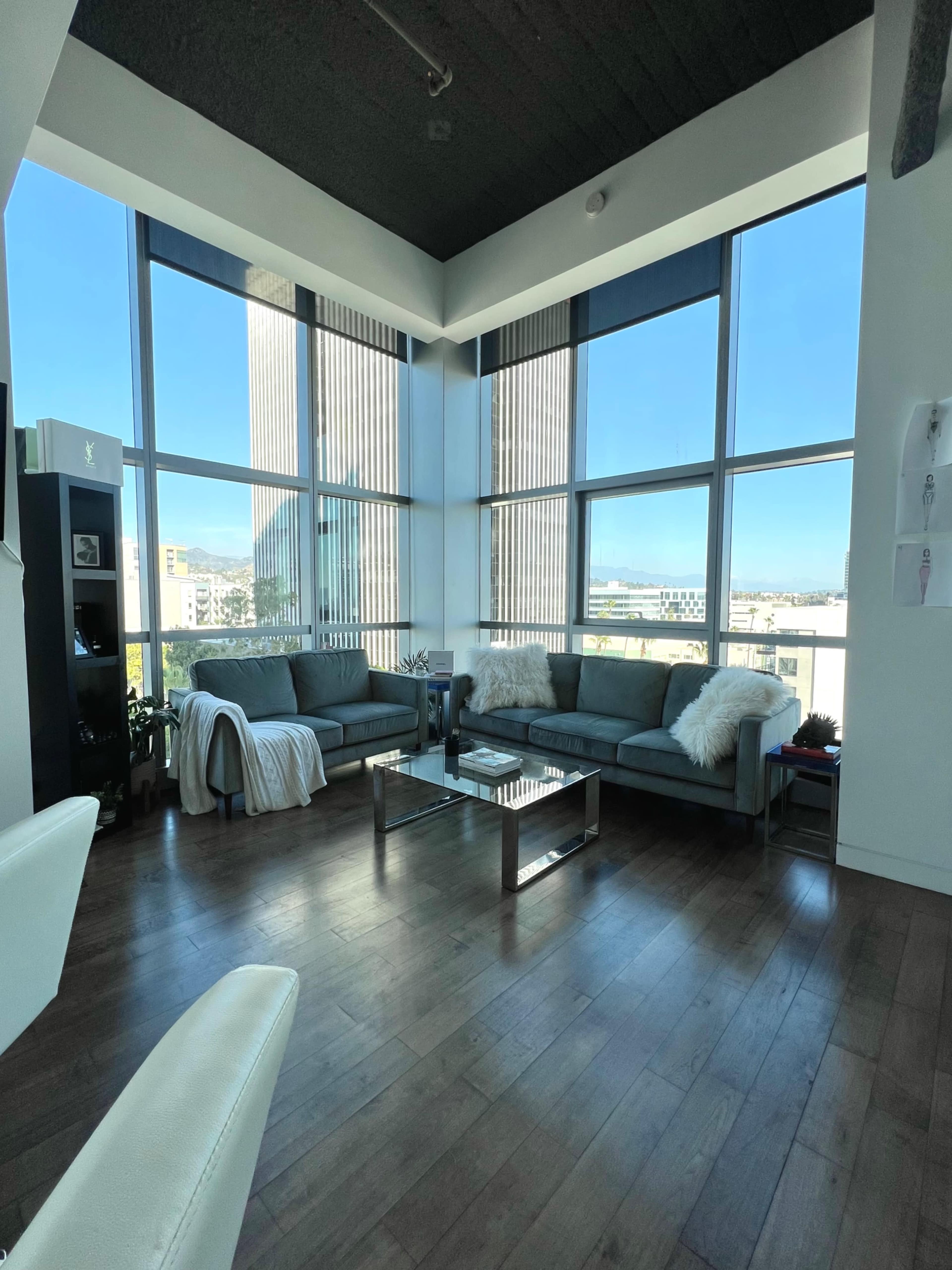 A modern living room features large windows with a view of city buildings, two sofas, a coffee table, and hardwood flooring.