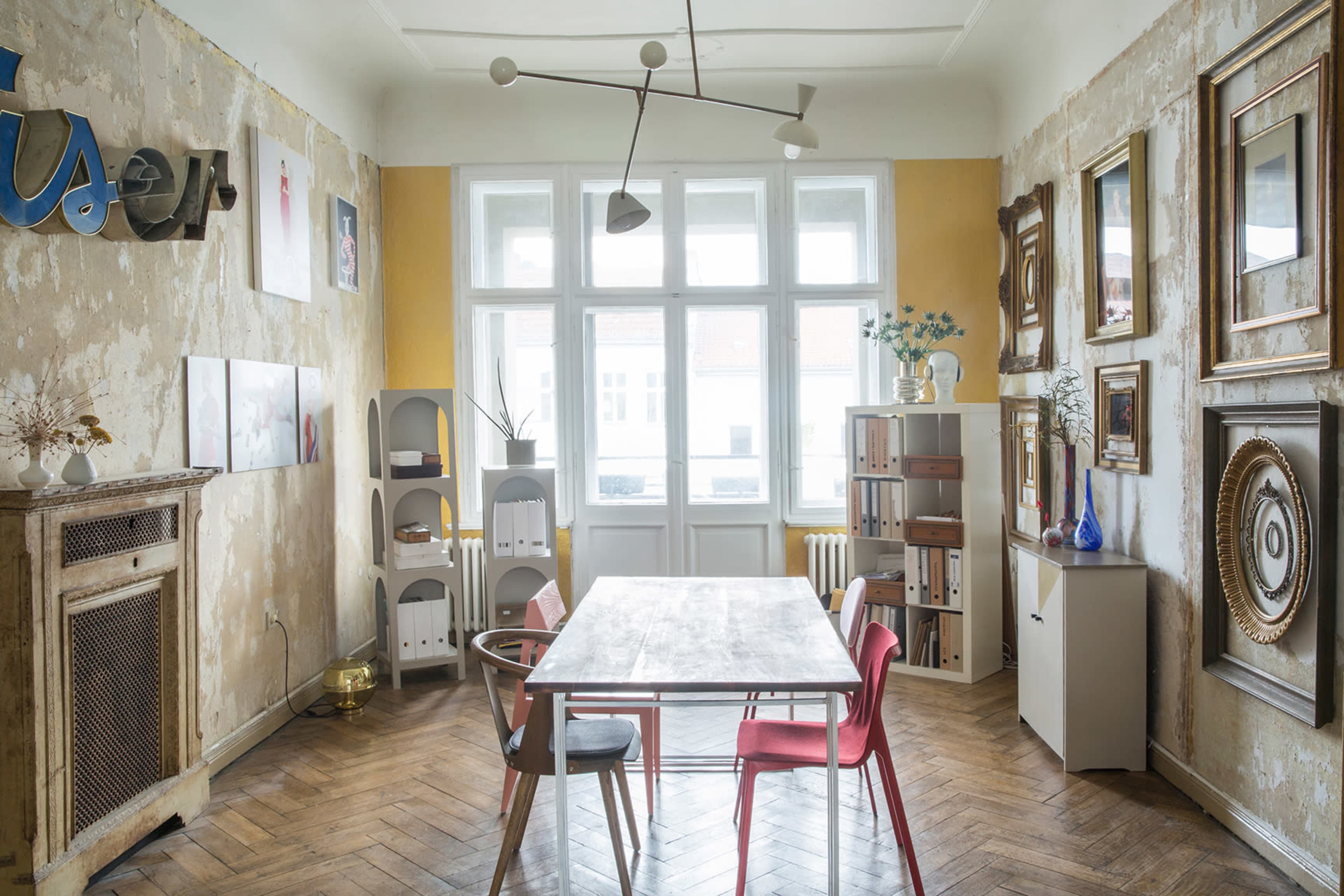 The image shows a room with a wooden table and several chairs, surrounded by textured walls and various framed artworks.