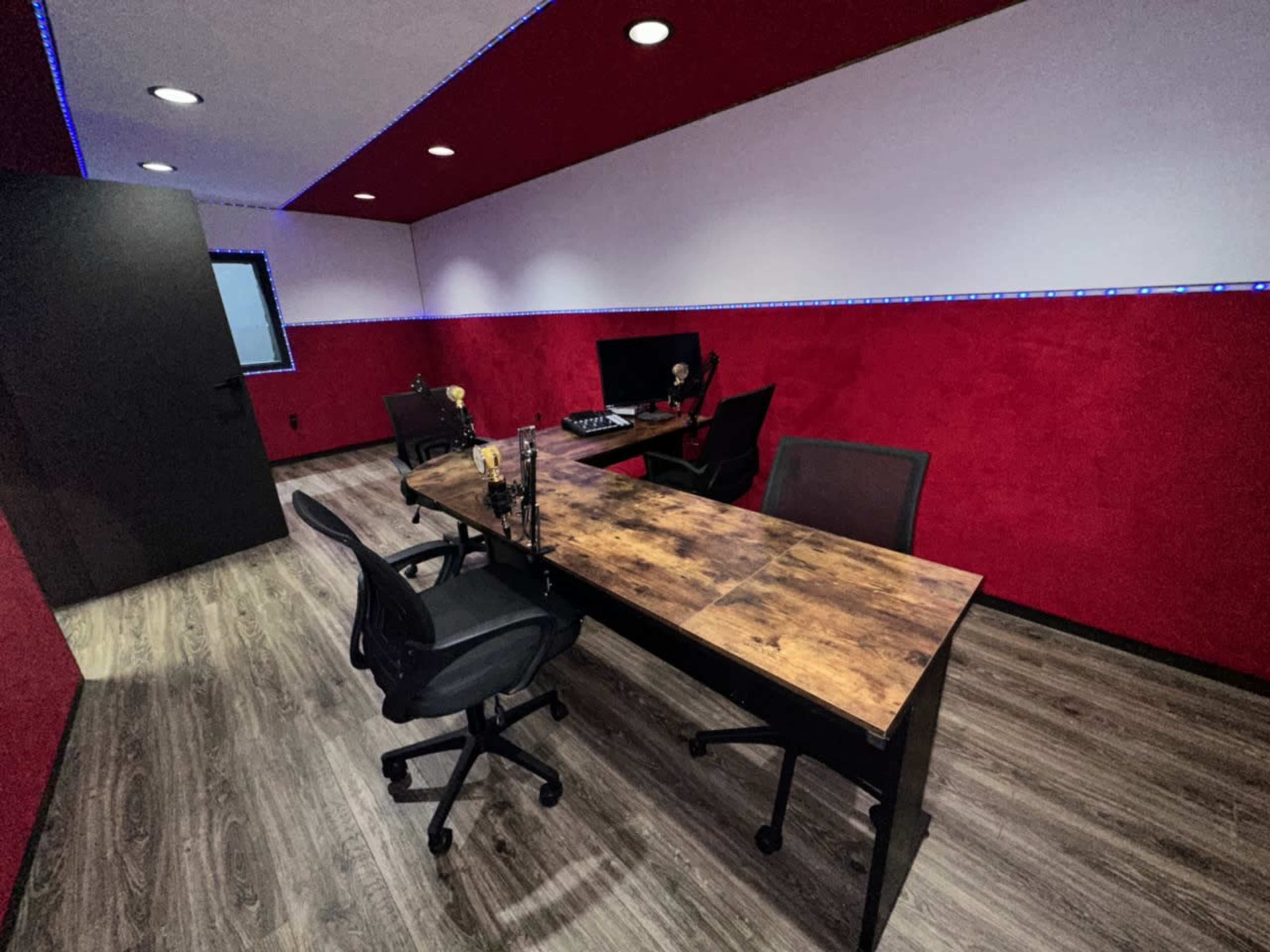 The image shows a modern office space with a wooden desk, two black office chairs, and red-accented walls illuminated by LED strip lights.