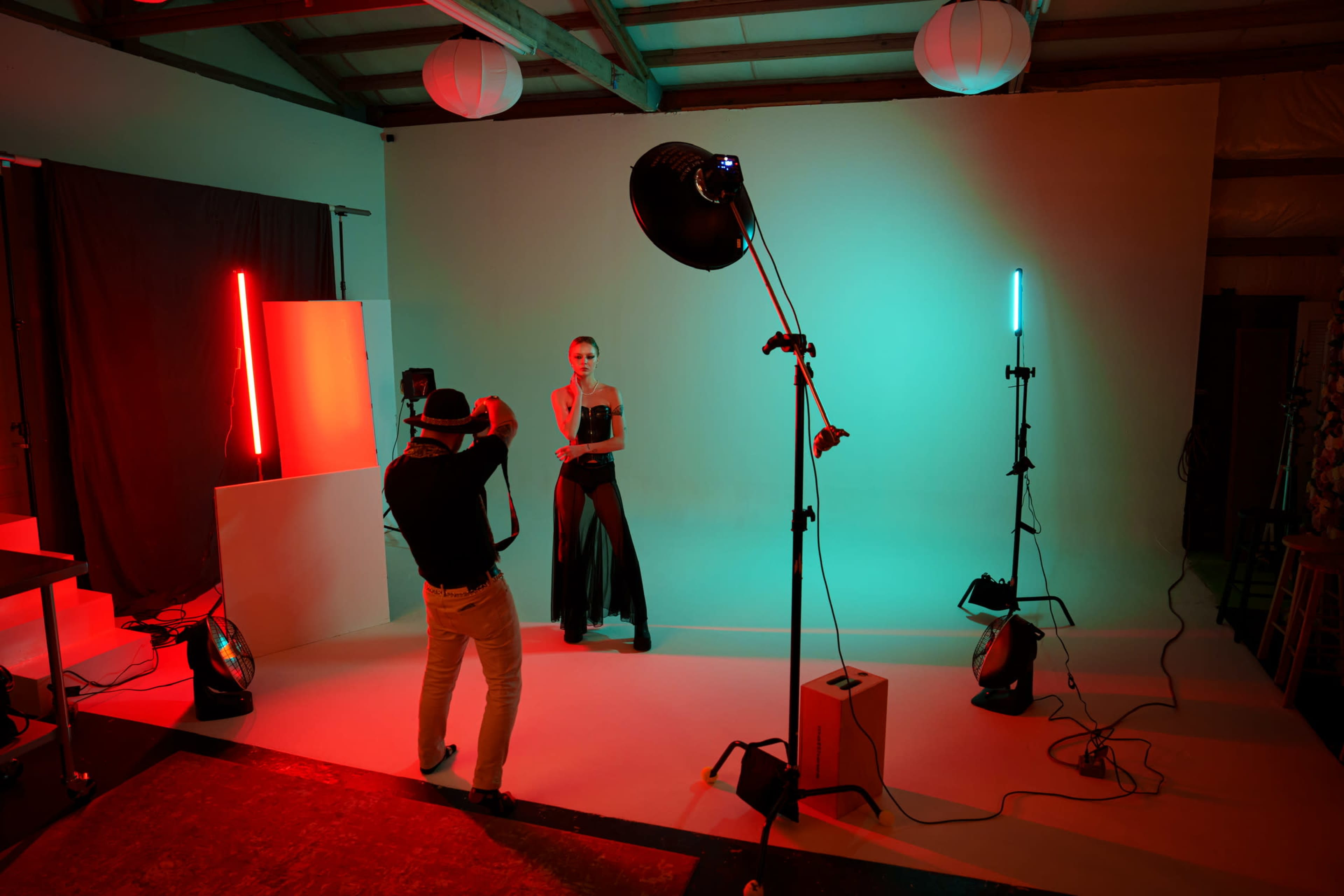 A photographer captures a model posing in a studio lit with colored lights against a neutral backdrop.