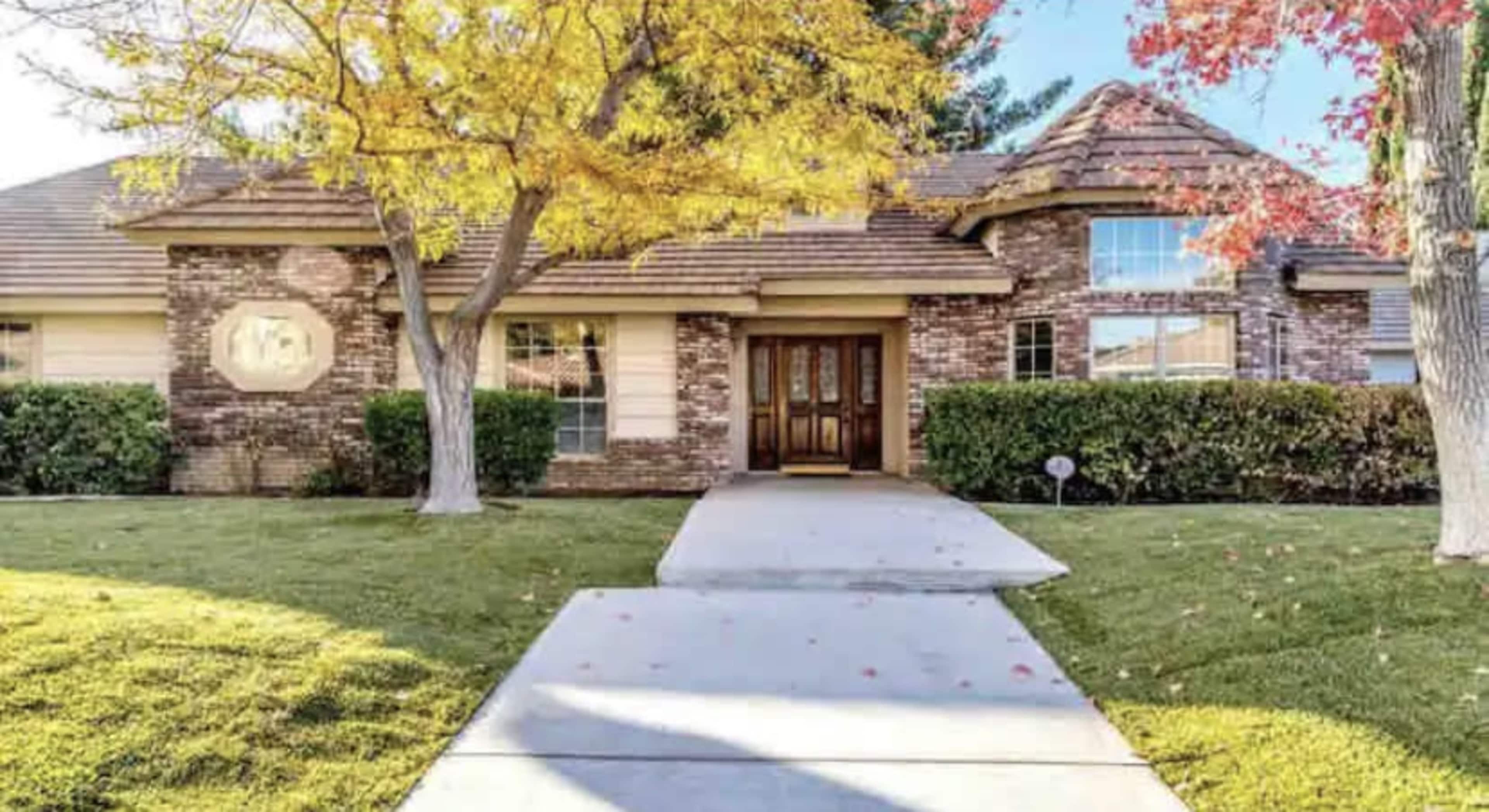 A brick house with a front yard featuring trees and a clear walkway leads to the entrance.