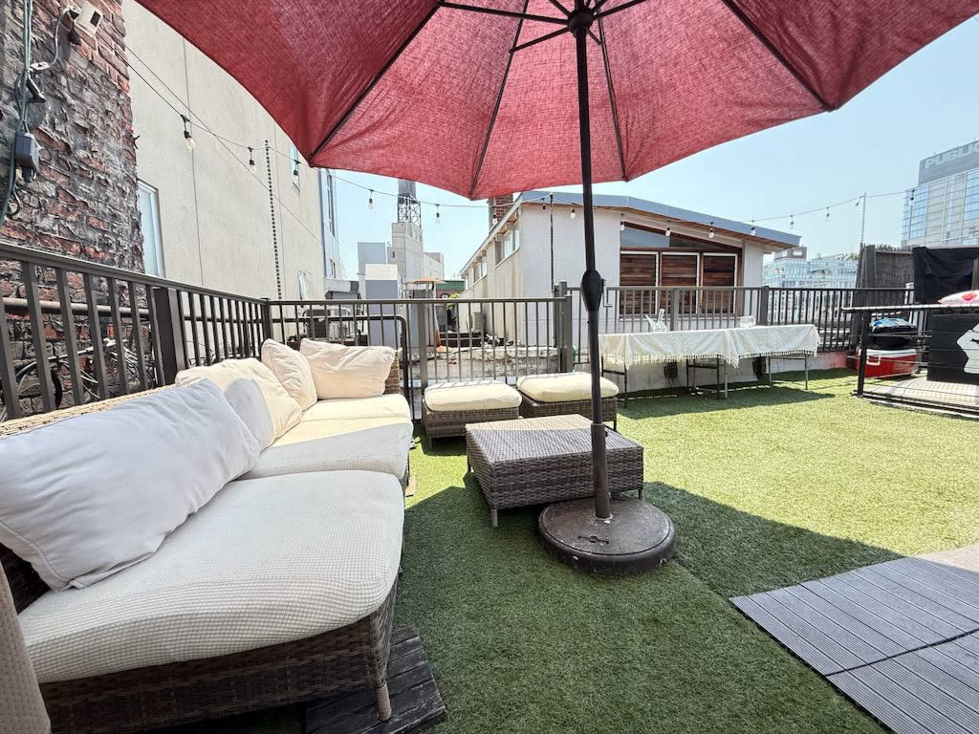 The image shows a rooftop patio area with a red umbrella, outdoor seating, and artificial grass.