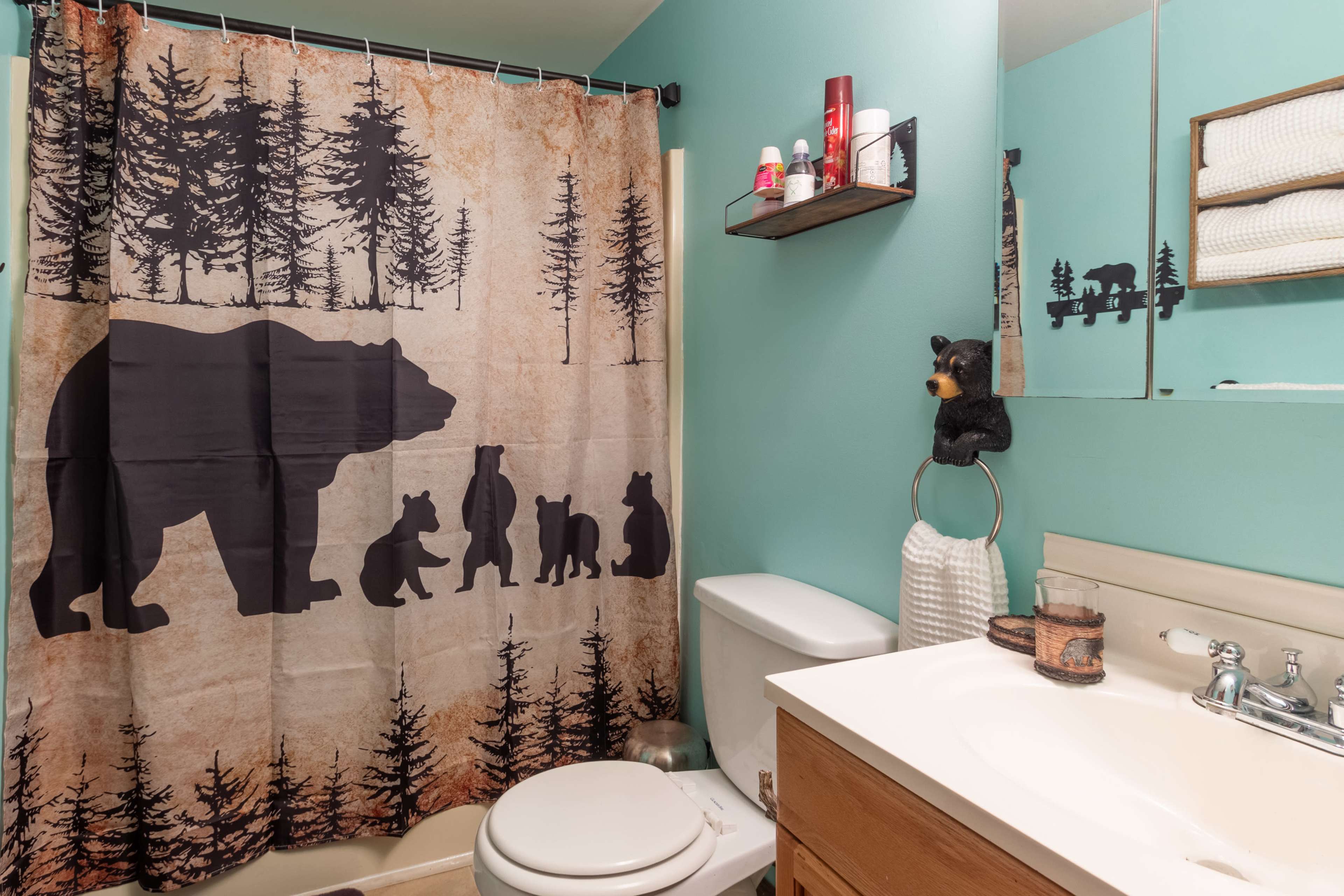 The bathroom features a bear-themed shower curtain, a white toilet, and a vanity with a mirror and shelf above it.