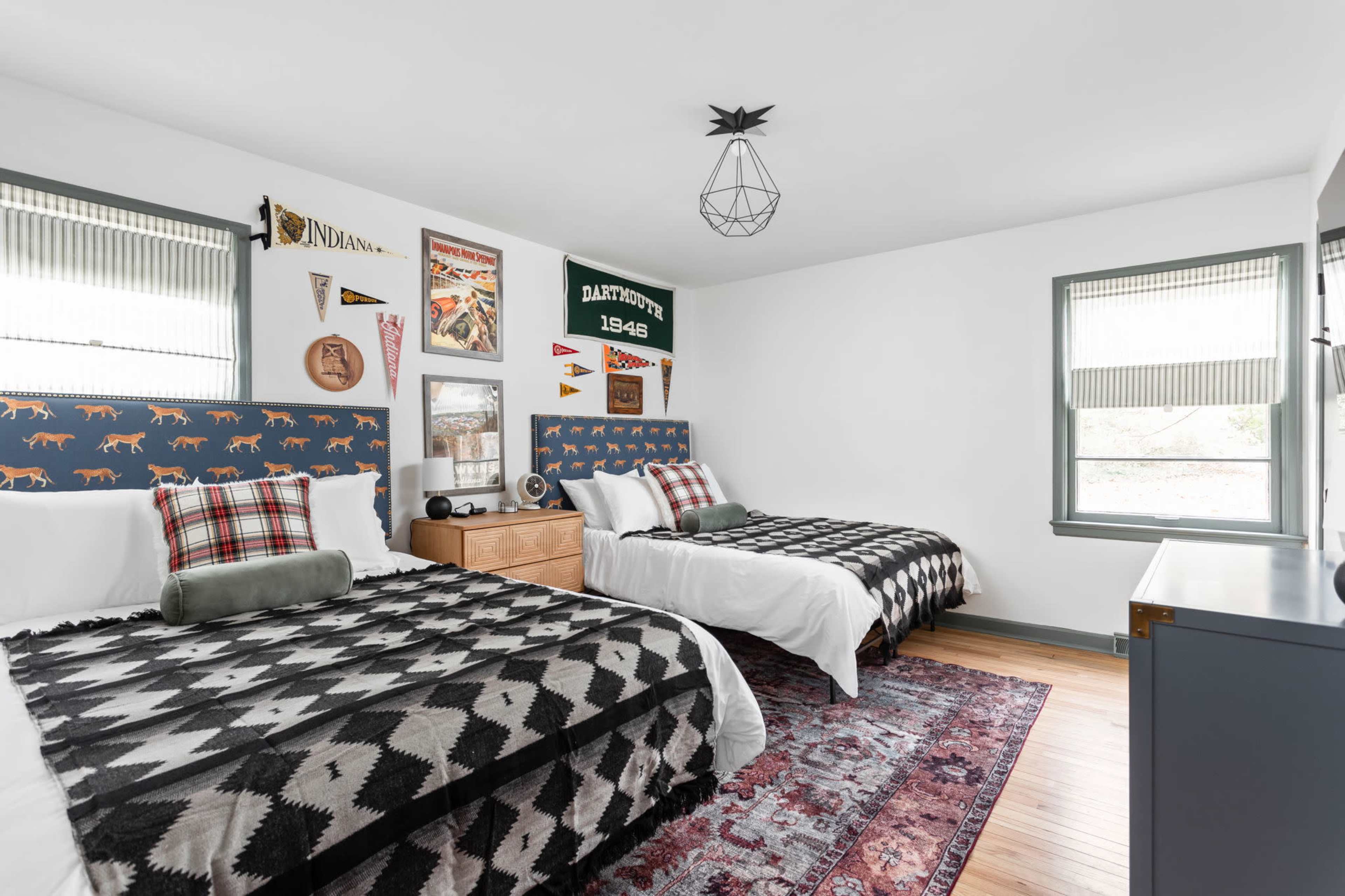 A brightly lit bedroom with two beds, each dressed in black and white patterned blankets, and adorned with vintage decor on the walls.