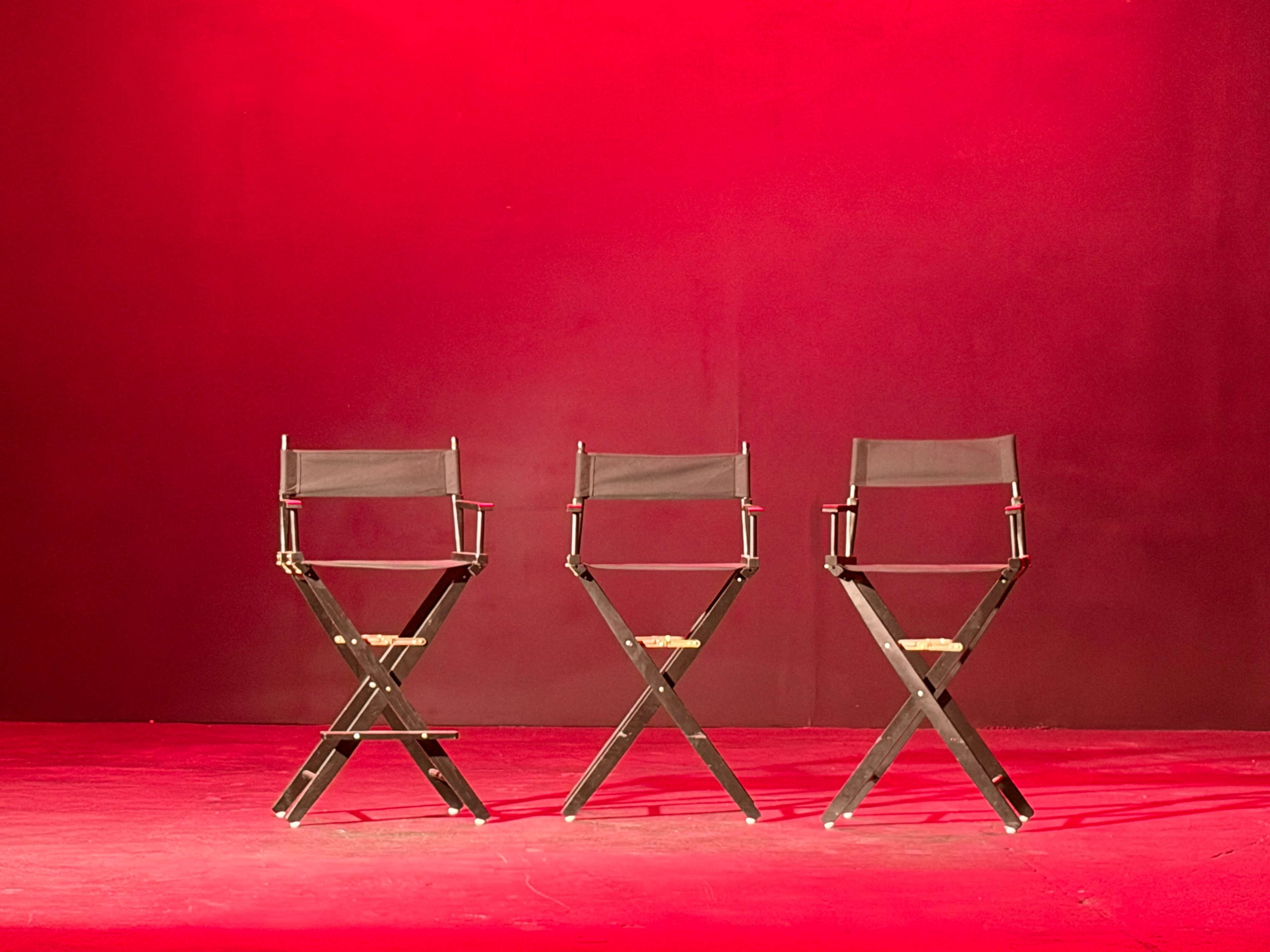 Three black director's chairs are arranged in a row on a red stage.