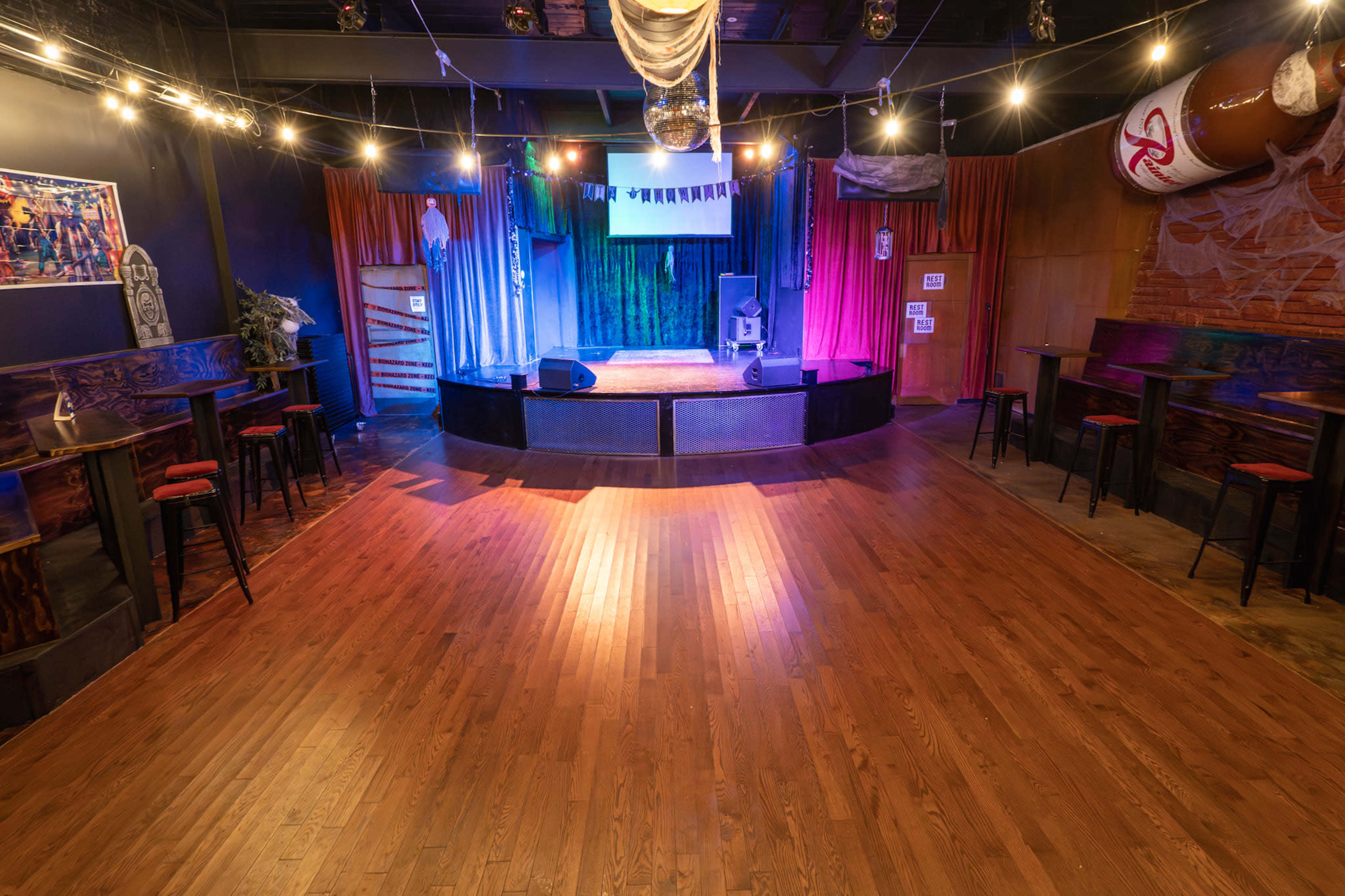 The image shows a performance stage in a venue, featuring a wooden floor, colorful curtains, and various lighting decorations.