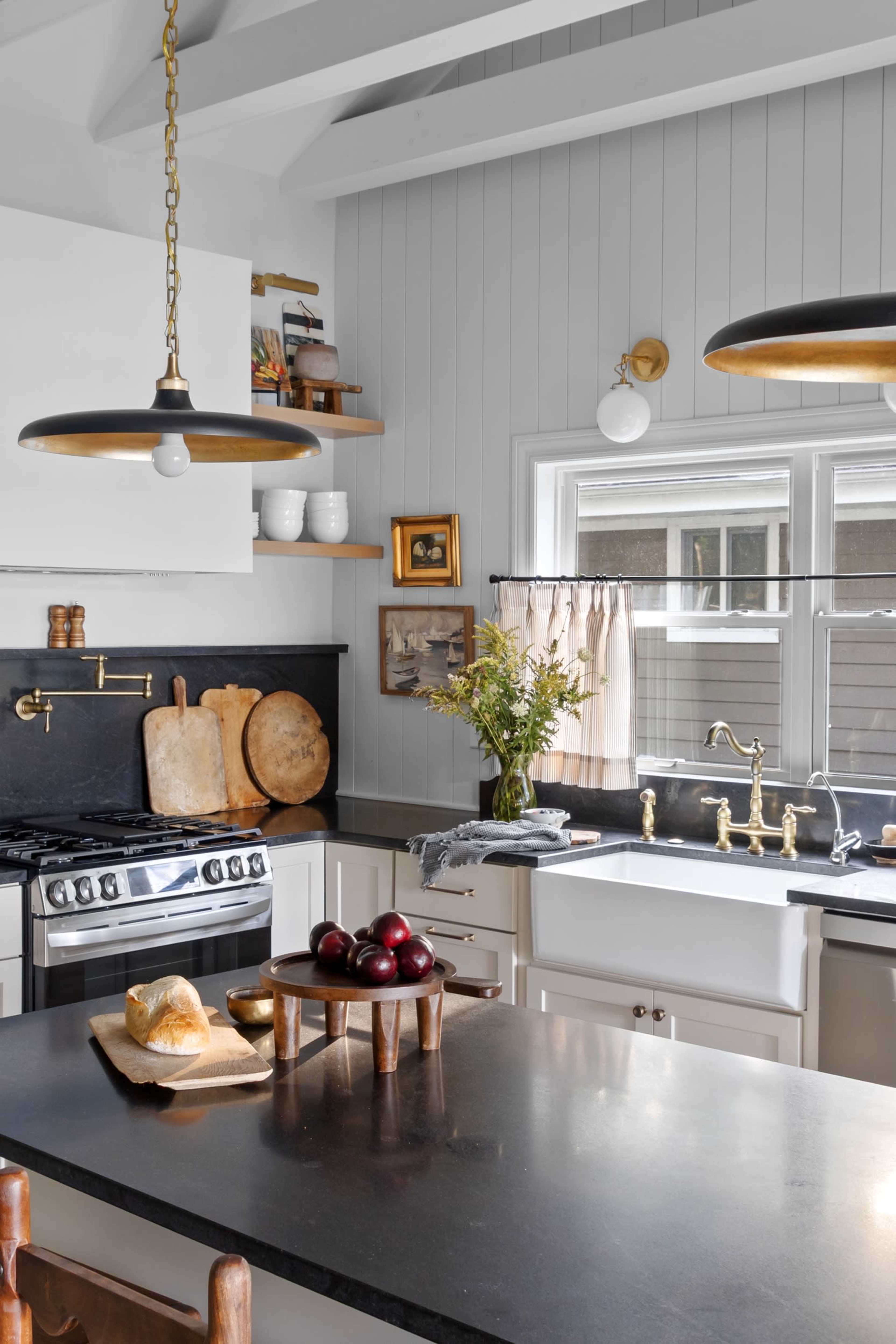 A modern kitchen features a central island with a fruit basket, sleek countertops, and a combination of dark and light cabinetry.