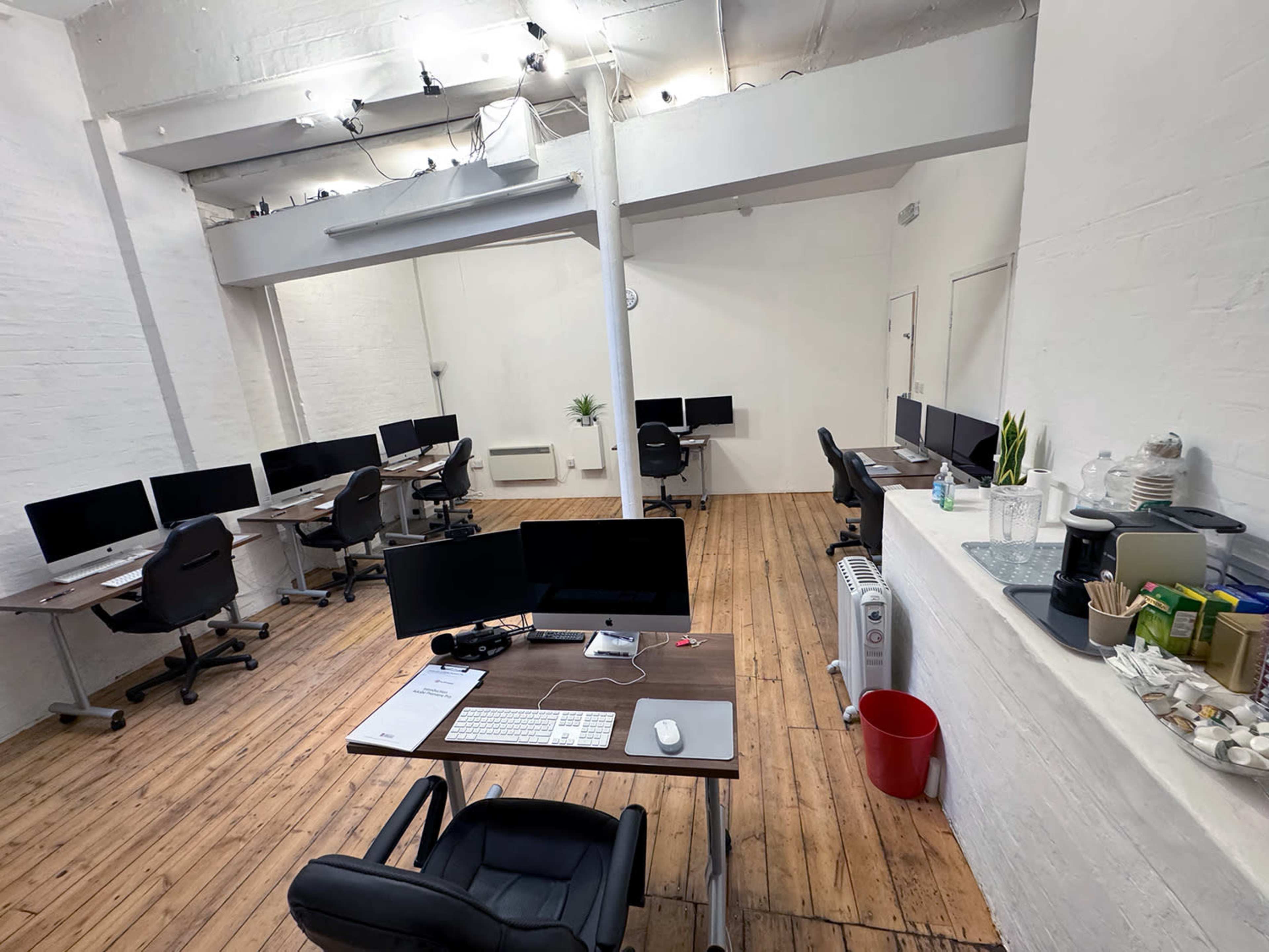 A spacious office layout with multiple workstations, each equipped with monitors, situated on wooden flooring.