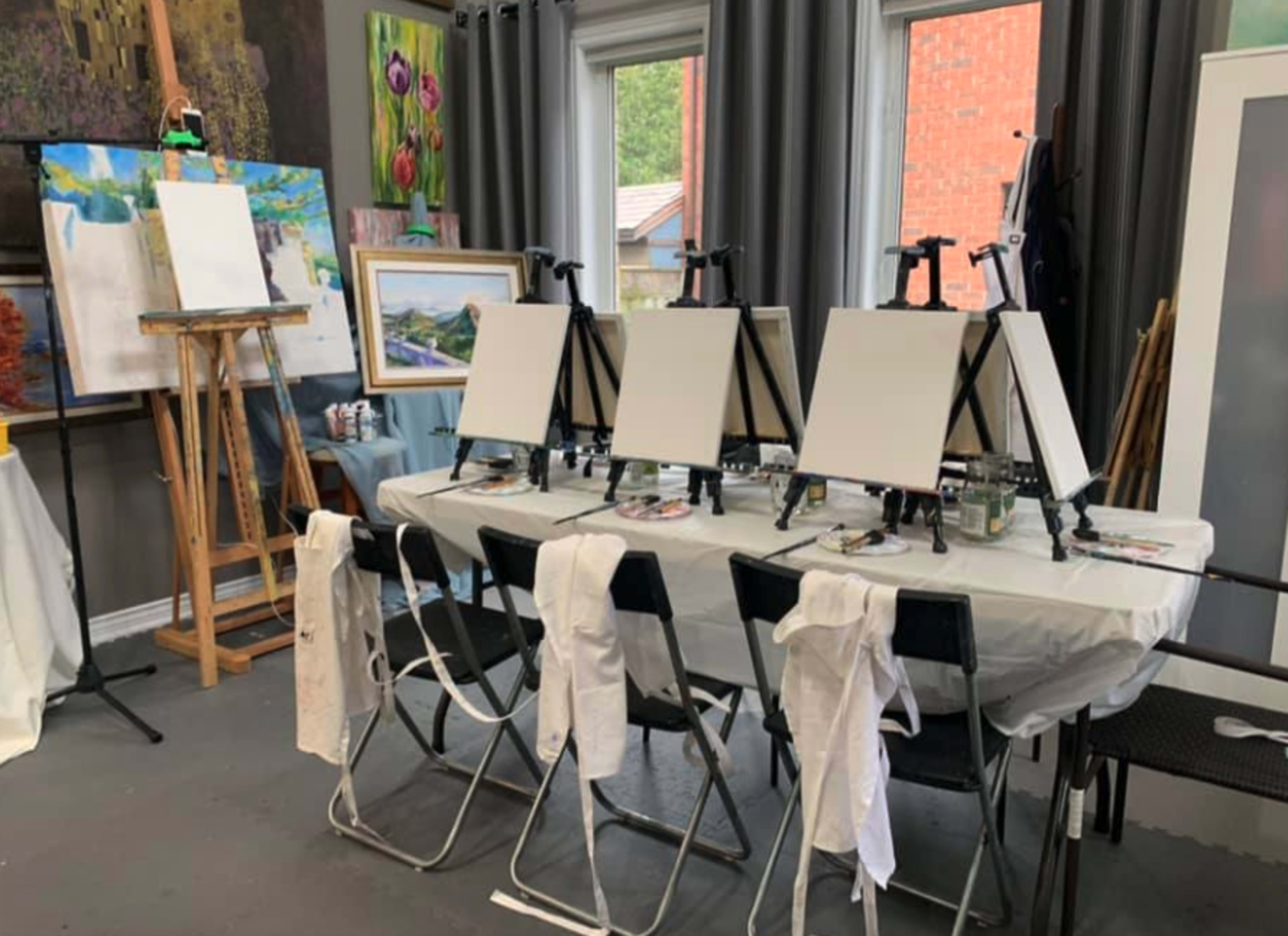 A row of empty easels is set up around a table covered with a white cloth in an art studio.