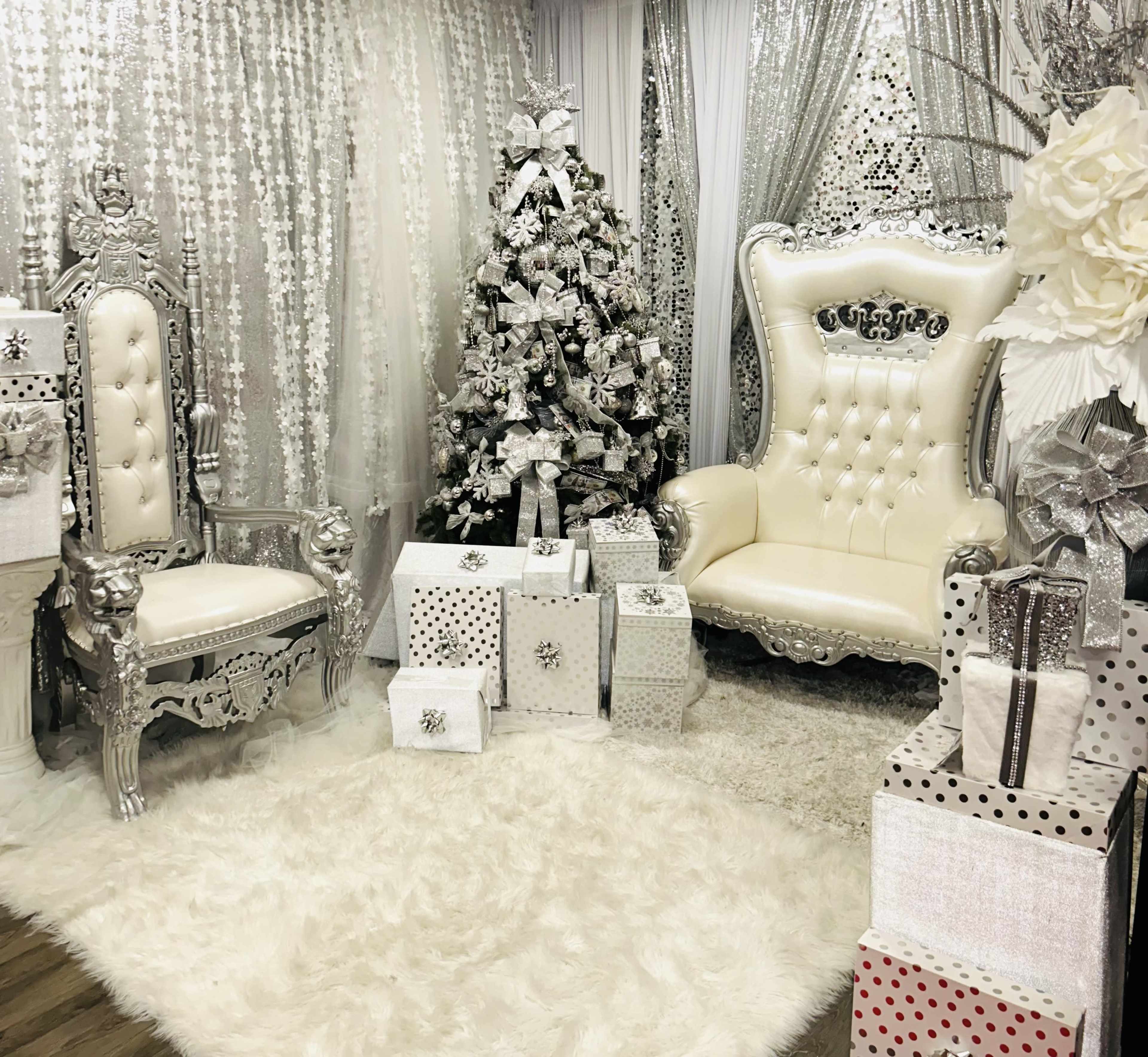 An elegantly decorated room featuring silver and white furniture, a Christmas tree, and wrapped presents.