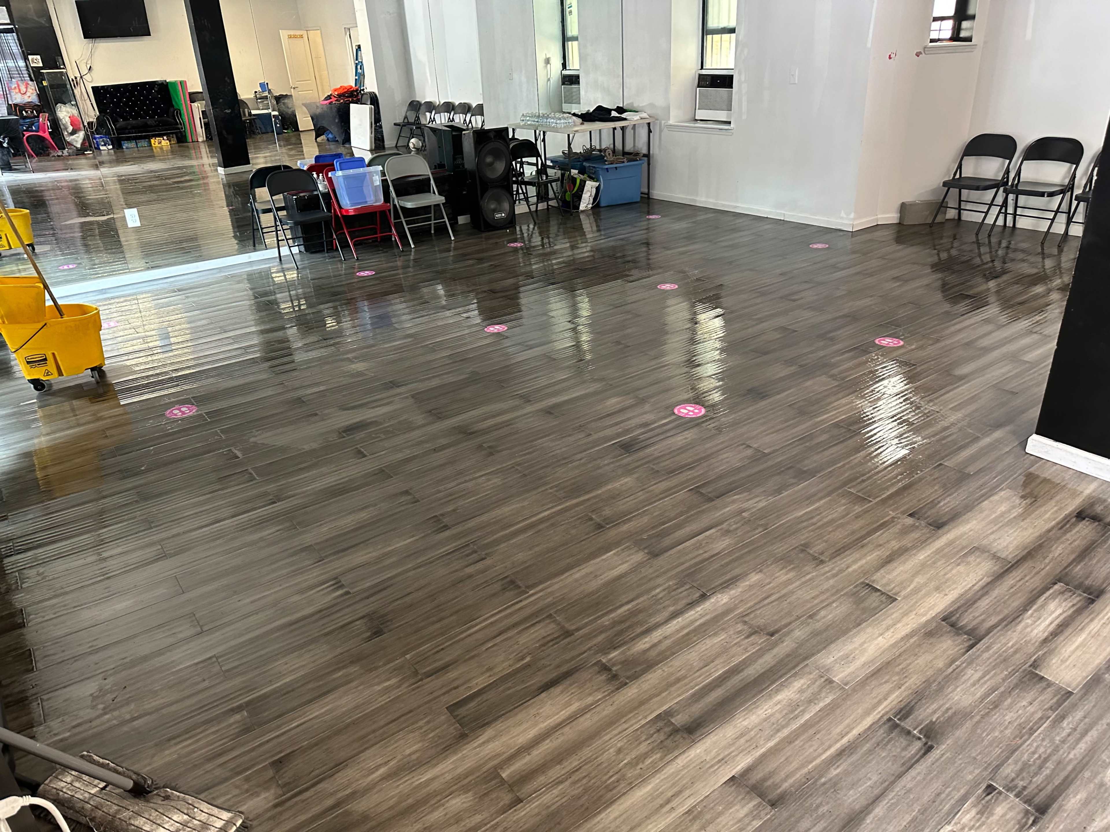 The image shows a spacious room with a shiny wooden floor, marked with pink circles, and furniture including chairs and carts in the background.