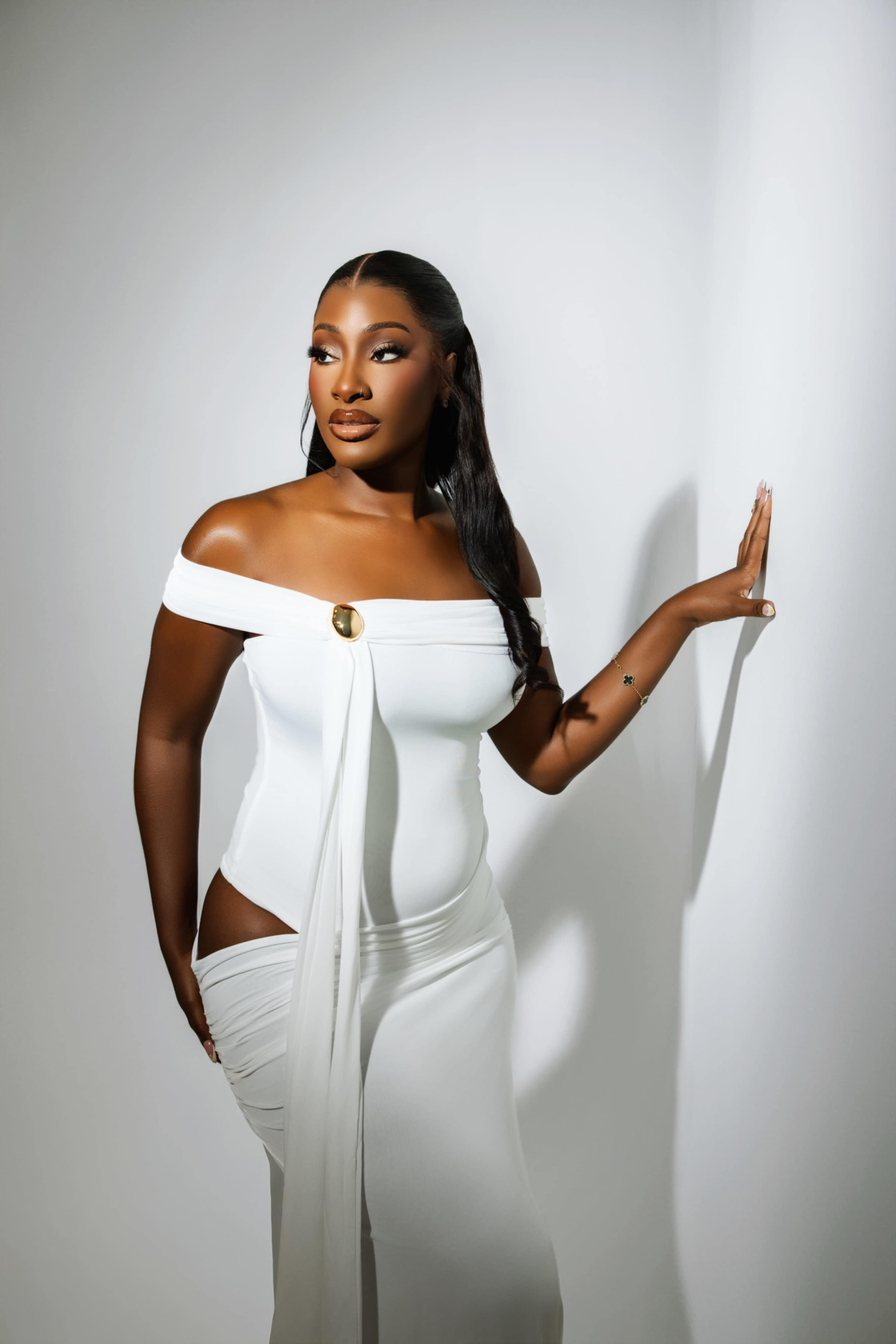 A woman in a white off-the-shoulder dress poses against a plain white background.