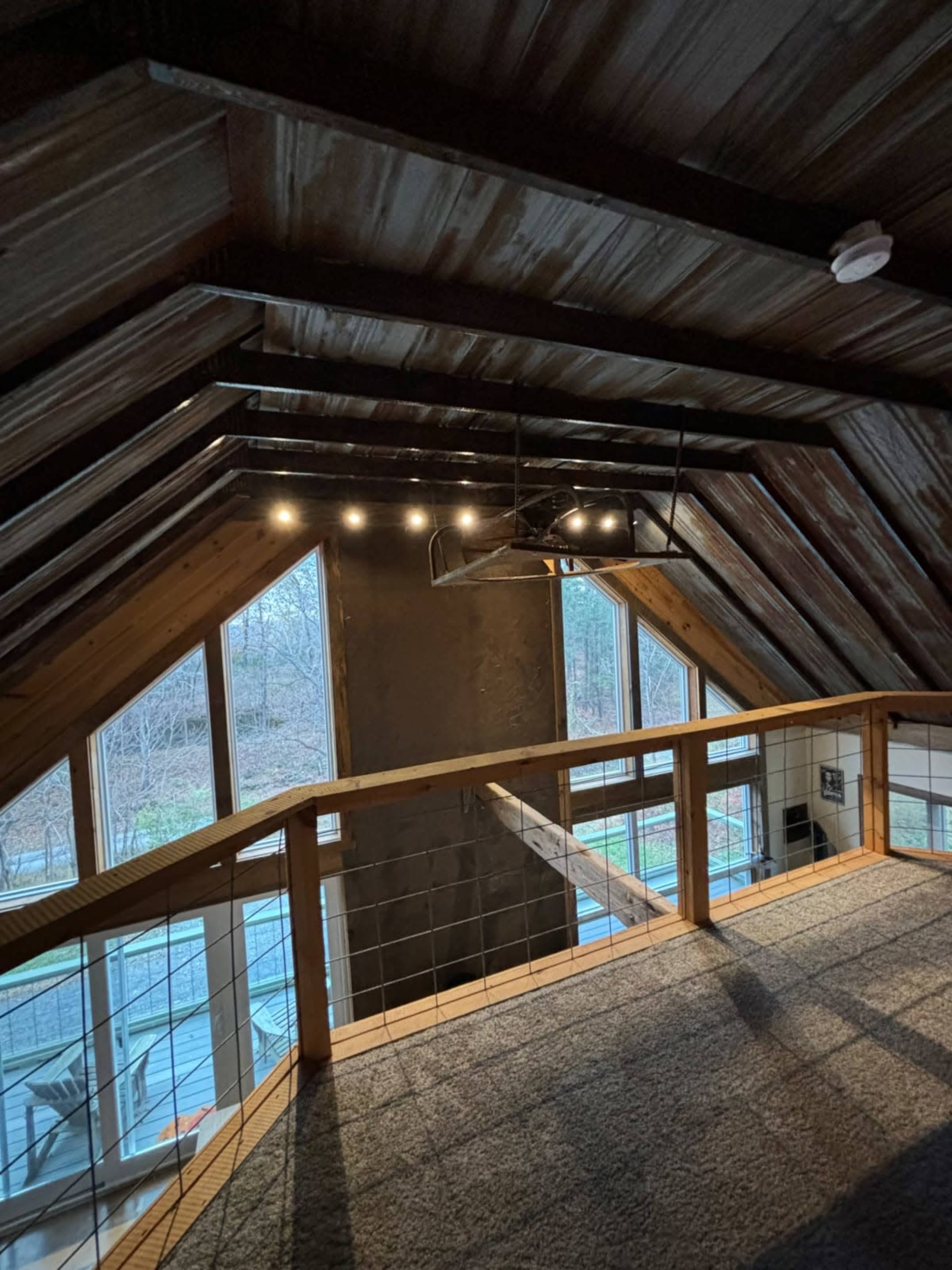 The image shows an attic space with a wooden railing, large windows, and a sloped ceiling, illuminated by overhead lights.
