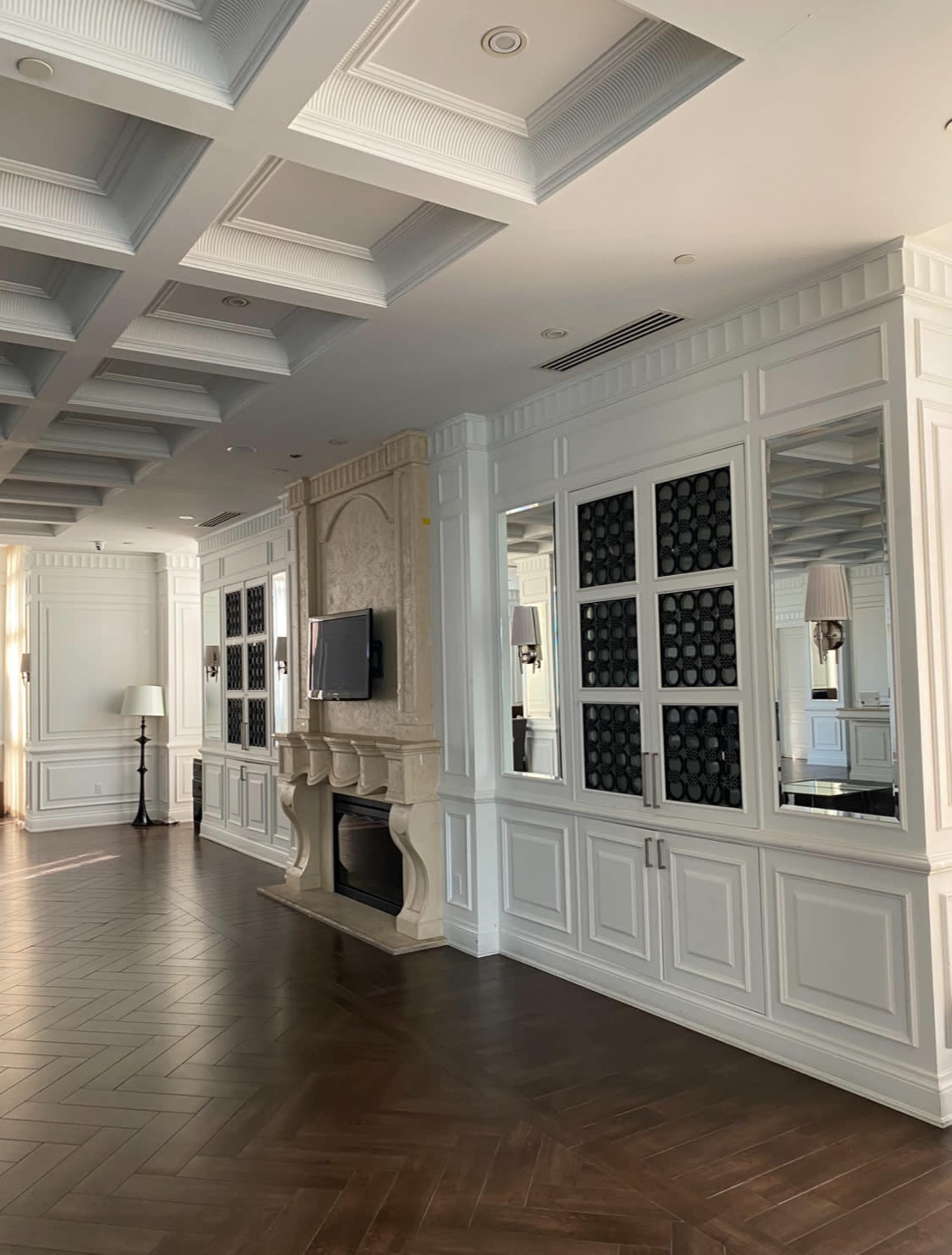 A well-lit interior space featuring white paneling, a fireplace with a TV mounted above it, and large mirrored cabinetry along the walls.