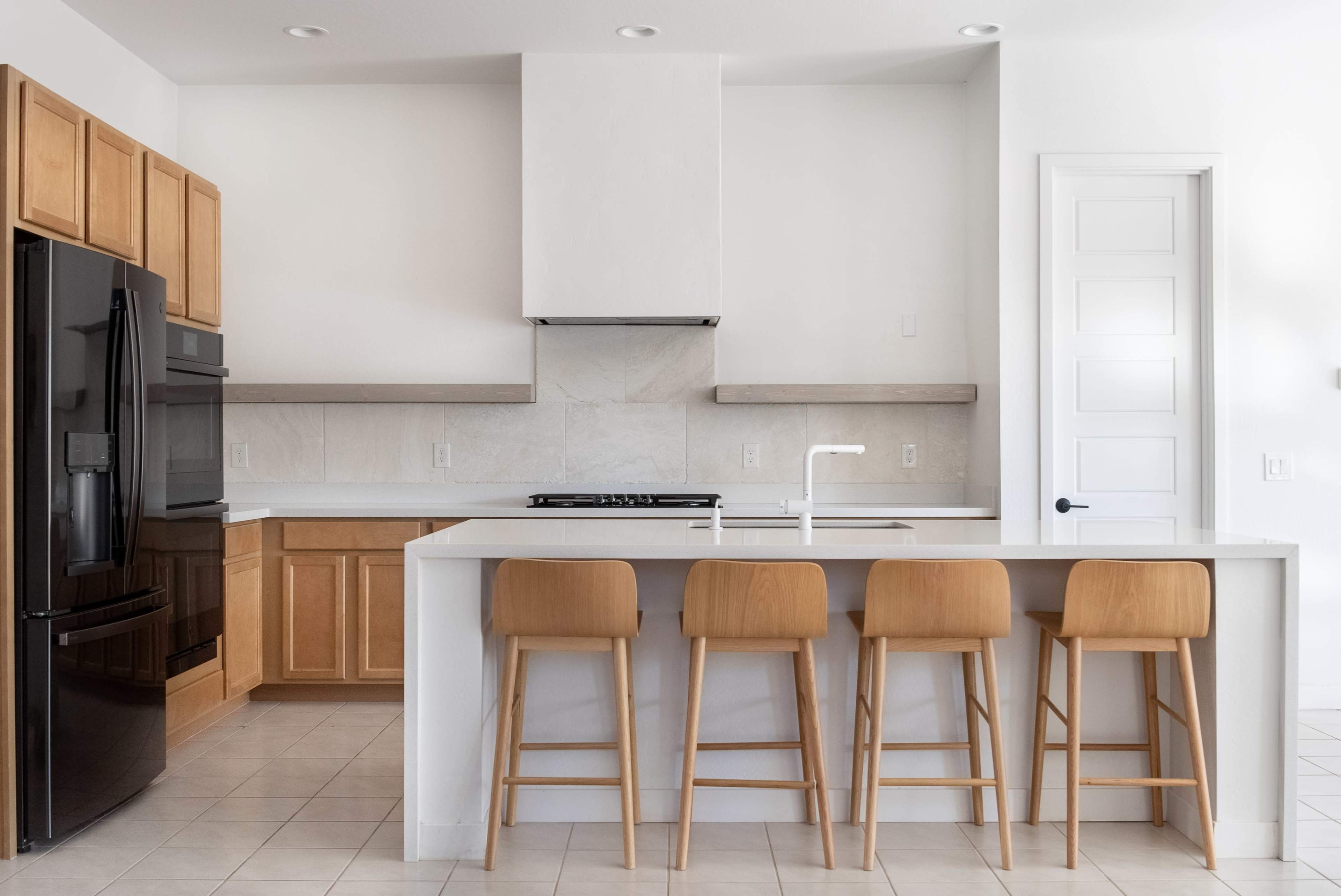 A modern kitchen features wooden cabinets, a black refrigerator, and a white island with four wooden bar stools.