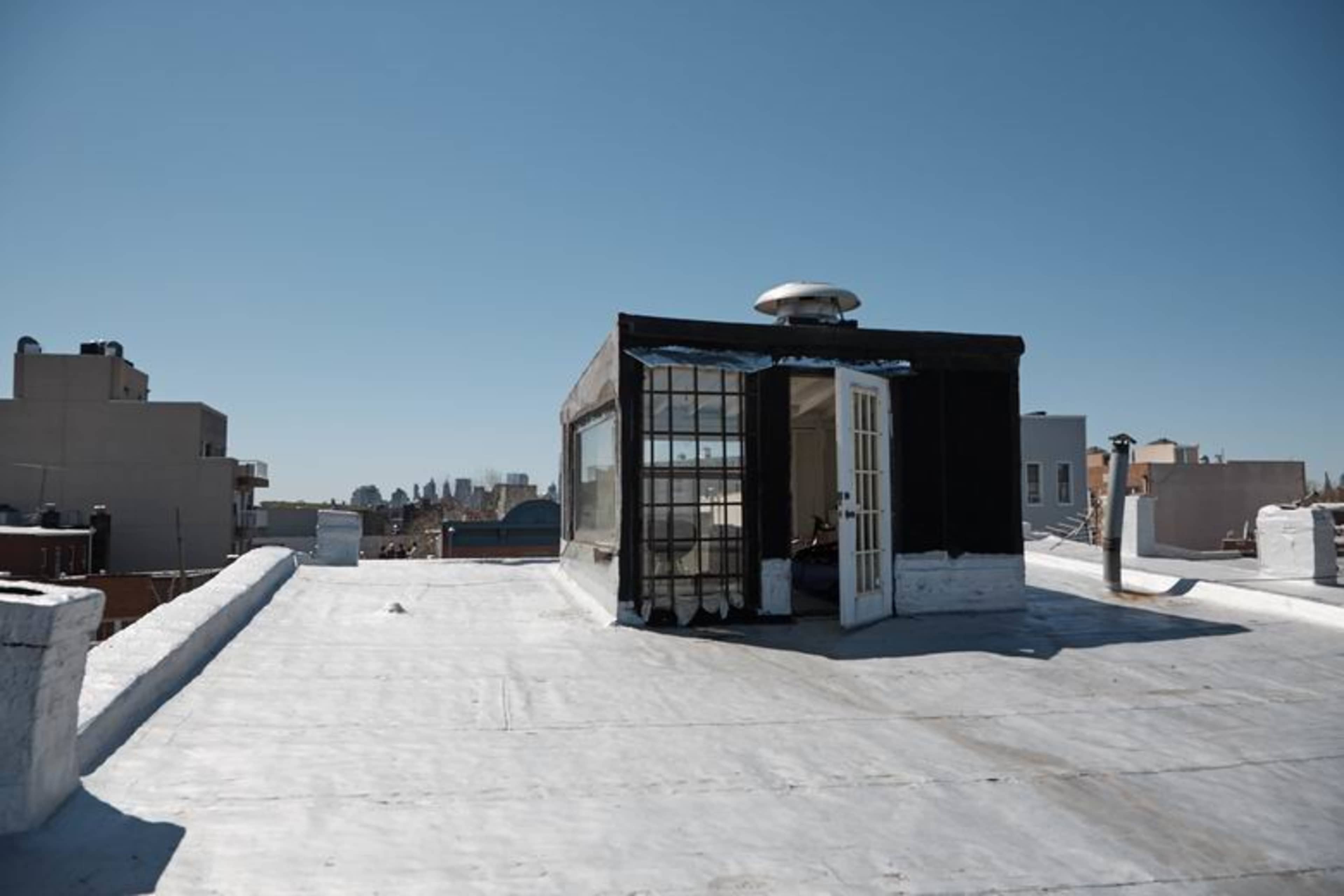 A black and glass rooftop structure is positioned on a flat, white rooftop, with a clear blue sky in the background.
