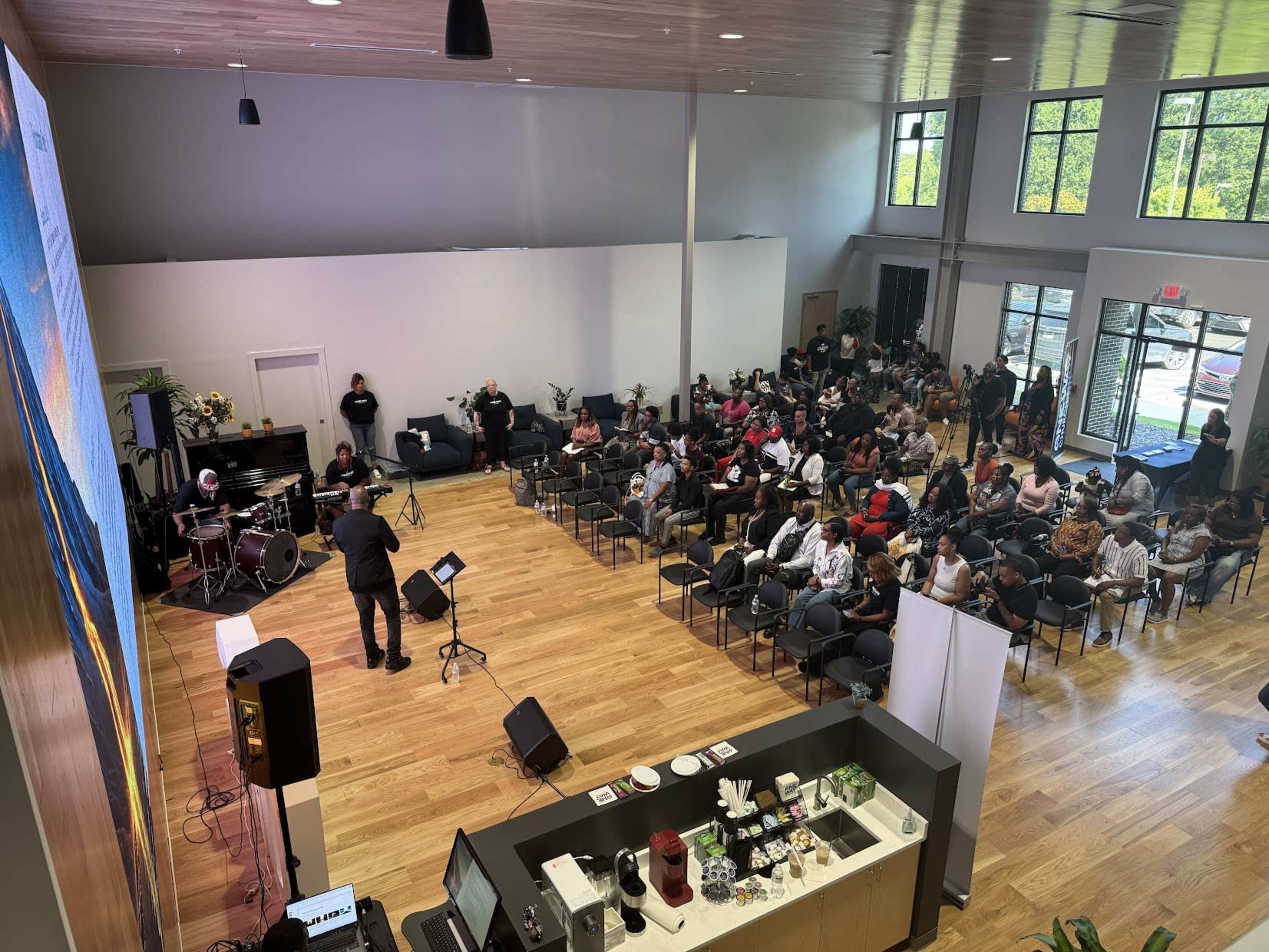 A musician performs on stage in a spacious hall filled with an audience seated in rows facing the performance area.