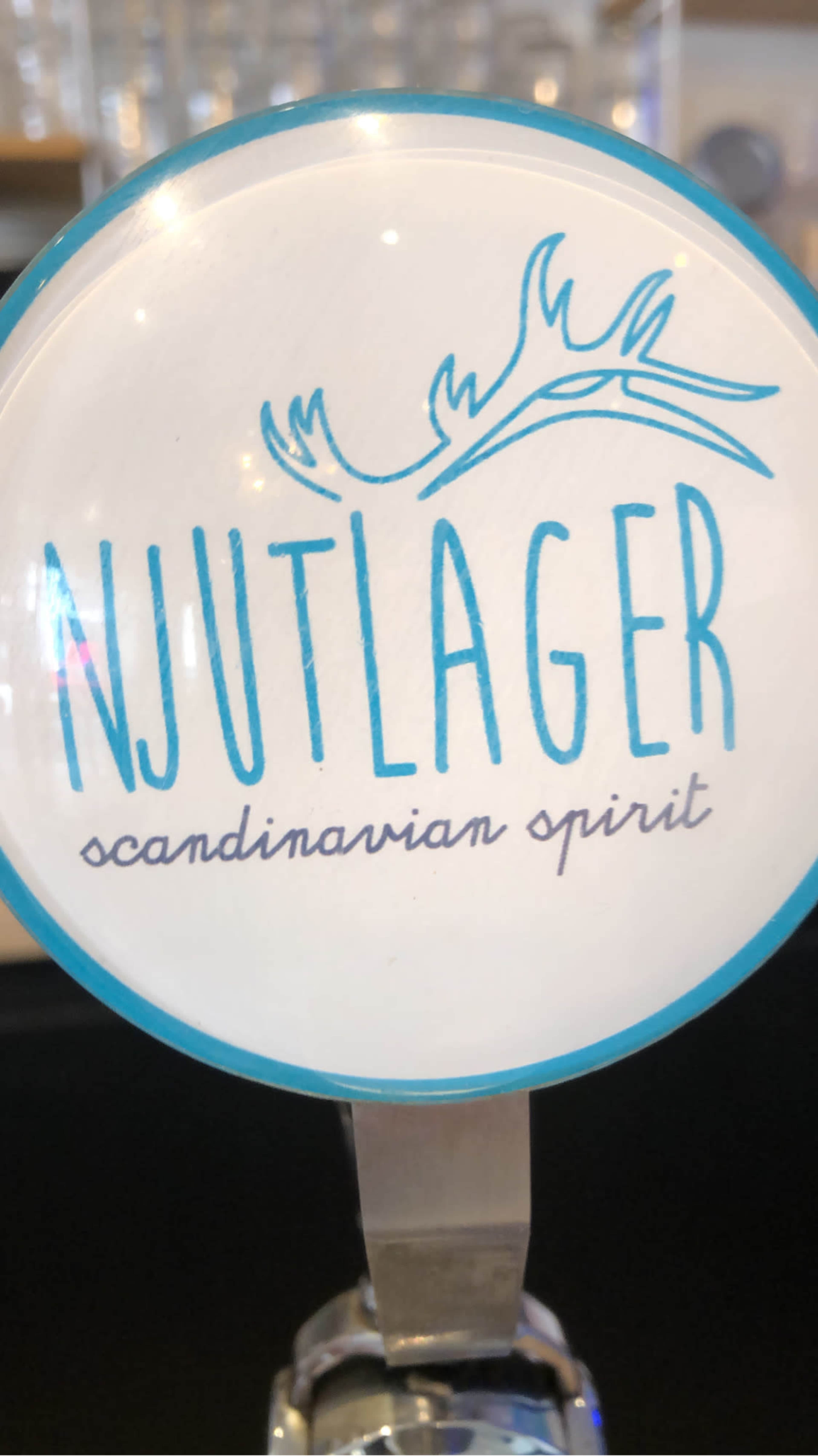 A circular tap handle featuring the word "NJUTLAGER" in prominent blue letters, accompanied by the phrase "scandinavian spirit" in a smaller font below.