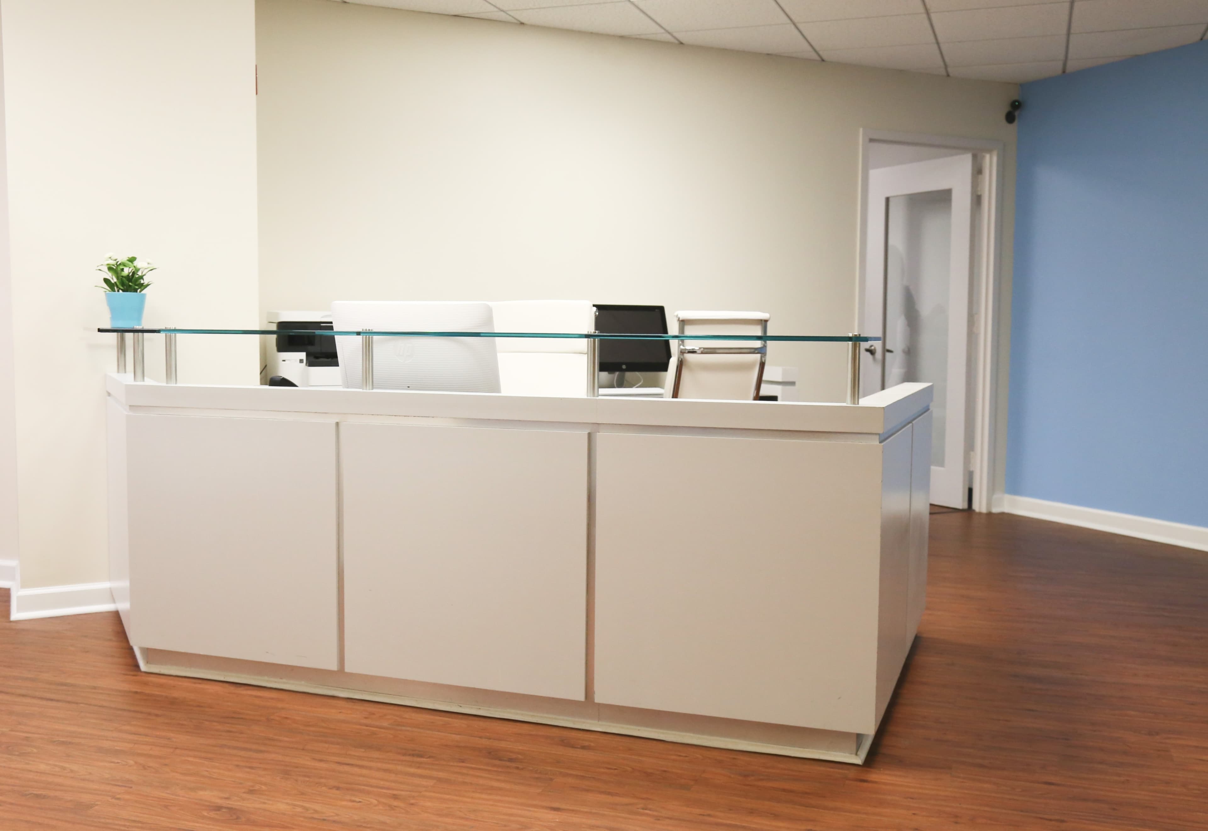 A modern reception desk in an office space with a computer setup and a small plant on top.