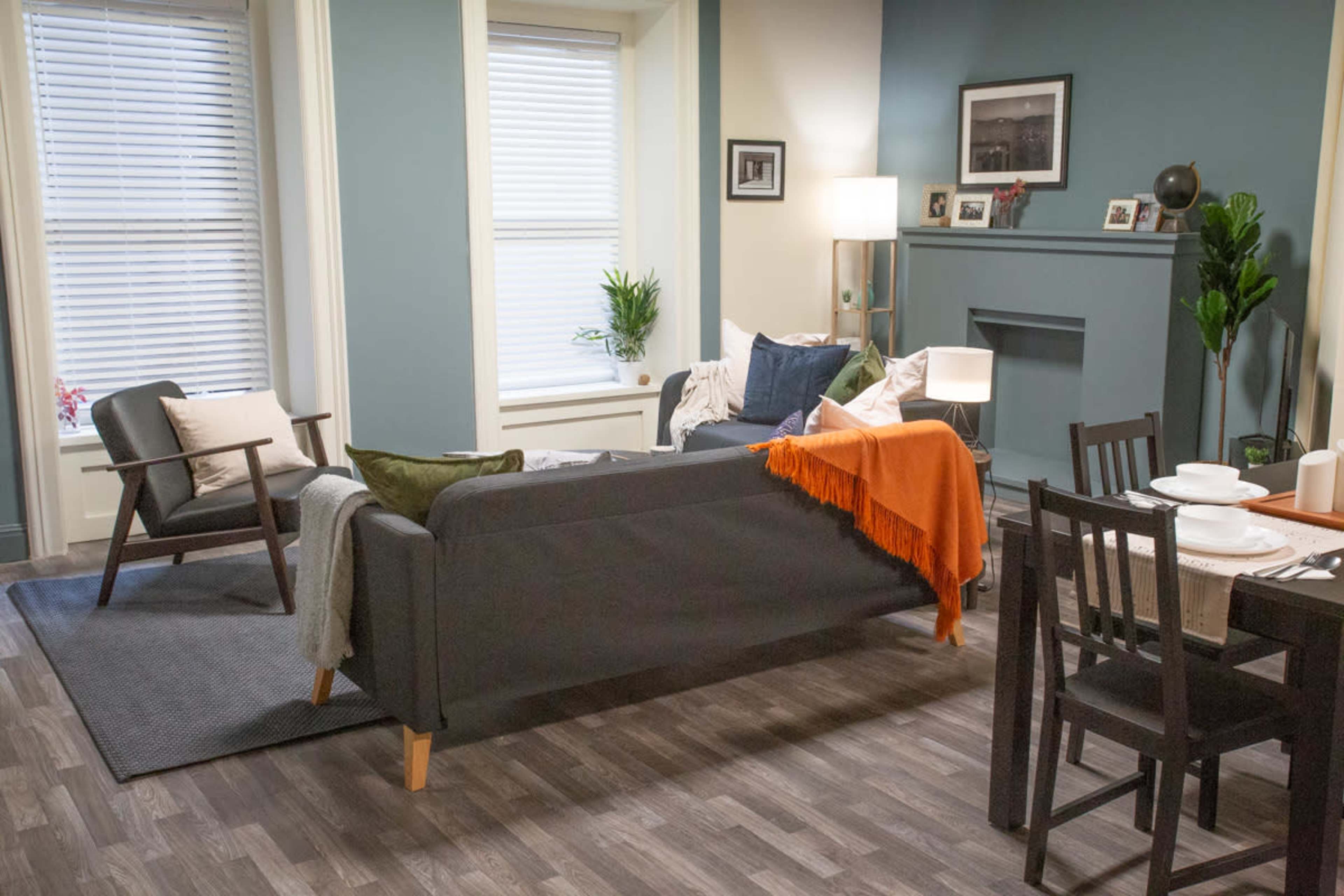 A living room with a couch, two armchairs, a dining table, and various decorative elements against a backdrop of light blue and beige walls.