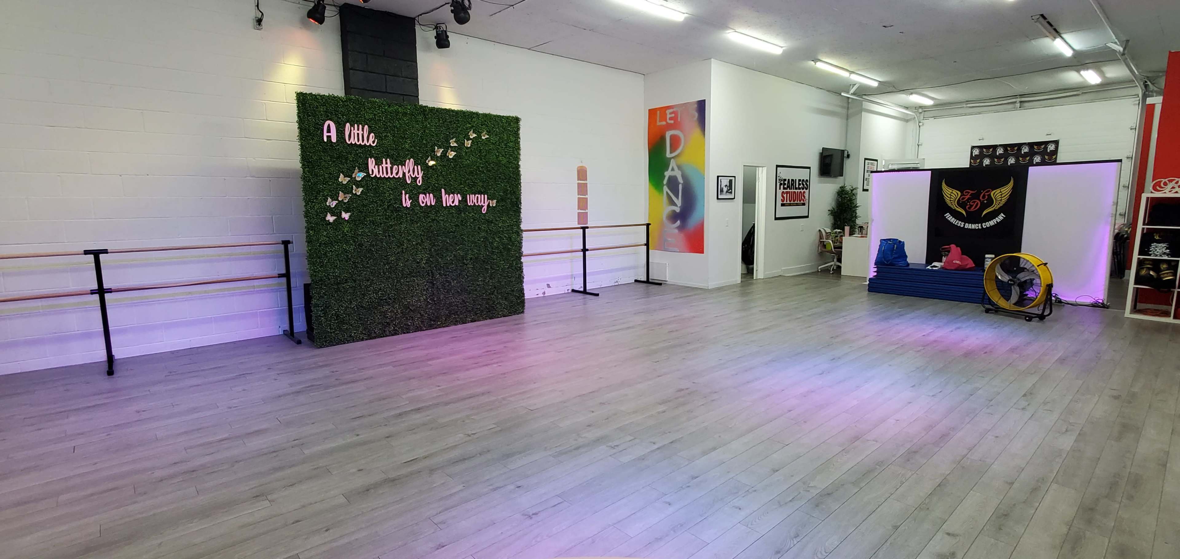 The image shows a dance studio with a wooden floor, mirrored walls, and a green wall feature adorned with decorative text.