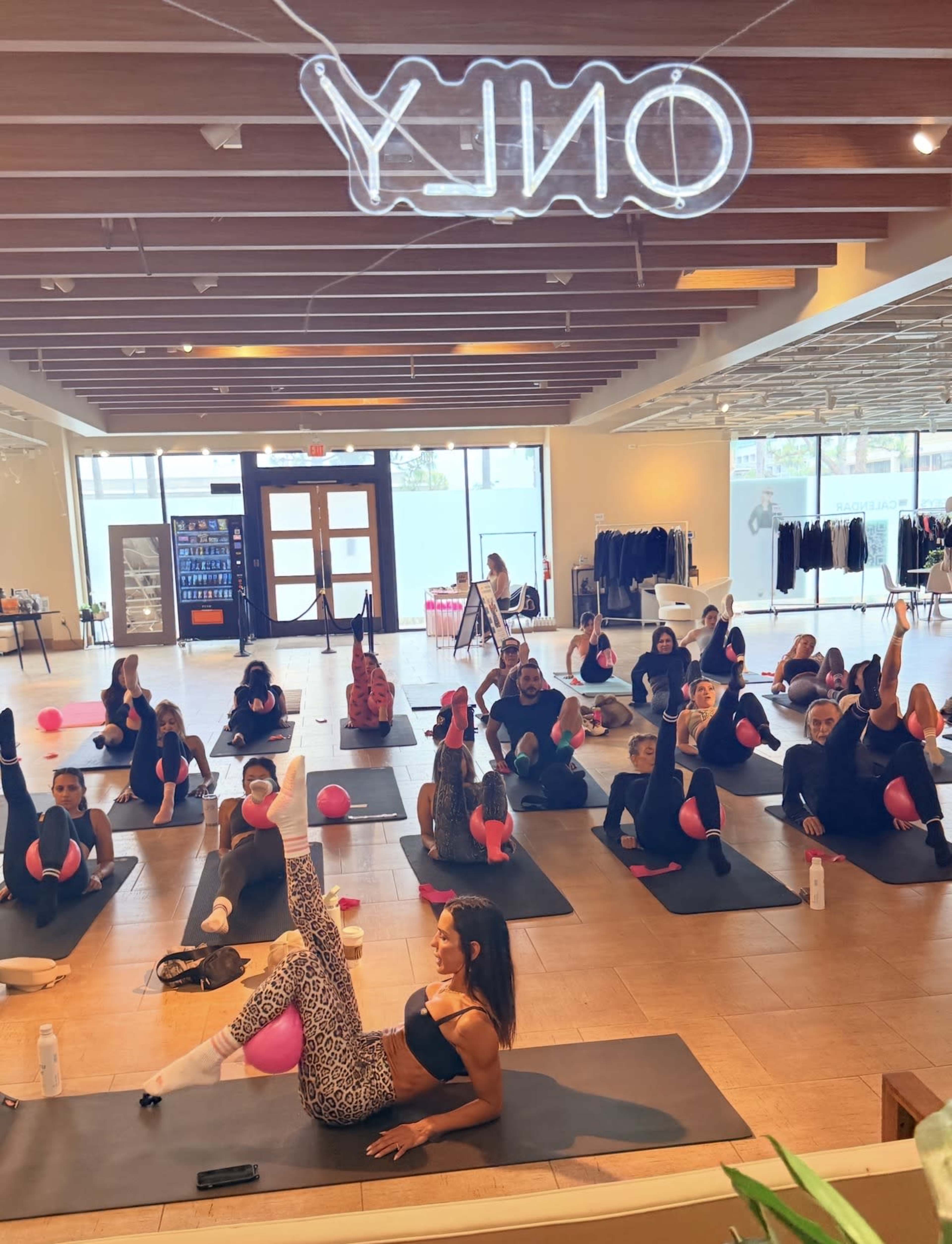 A group of people is participating in a fitness class, using exercise balls and yoga mats in a bright, spacious studio.