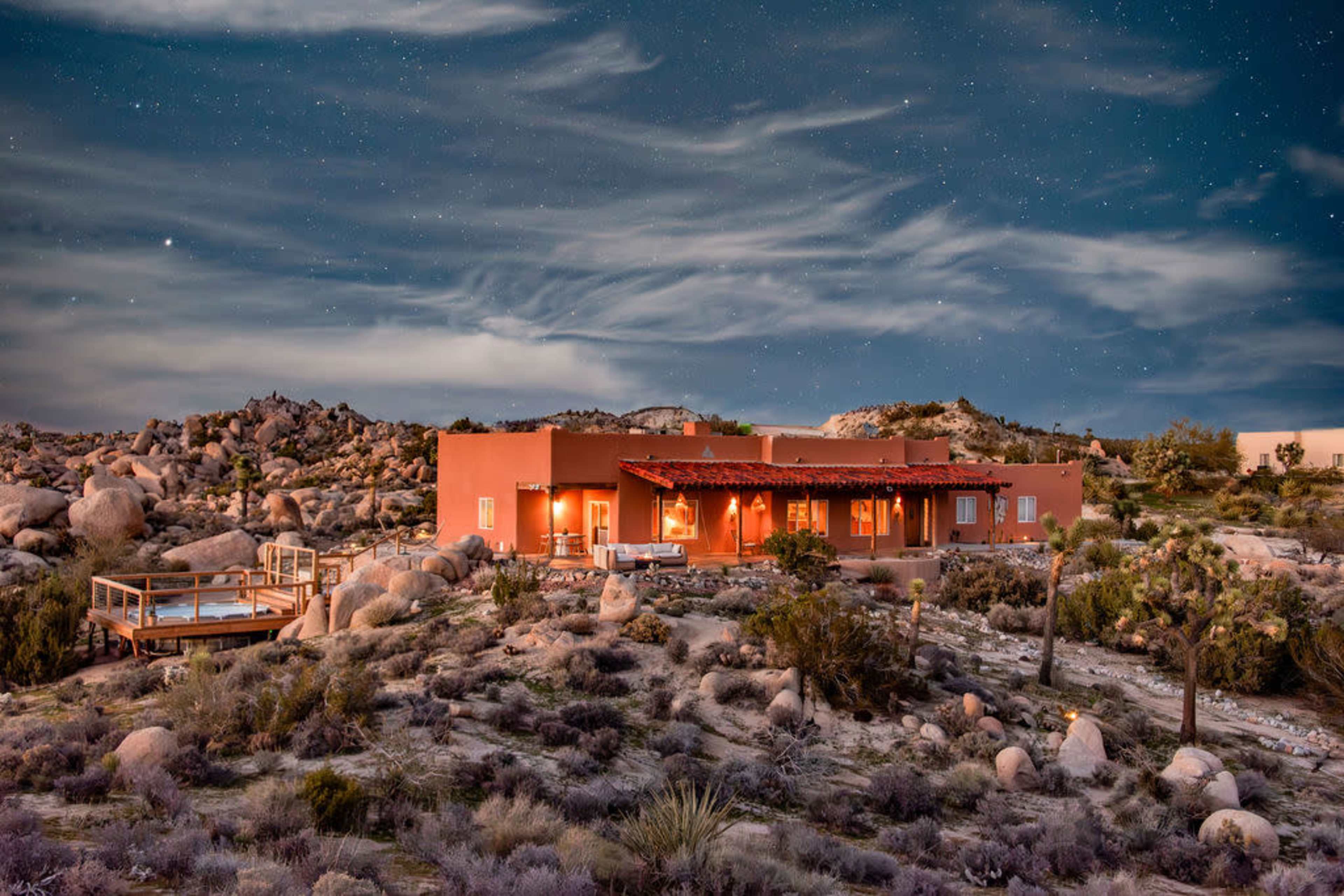 A southwestern-style house is situated among boulders and desert vegetation under a starry night sky.